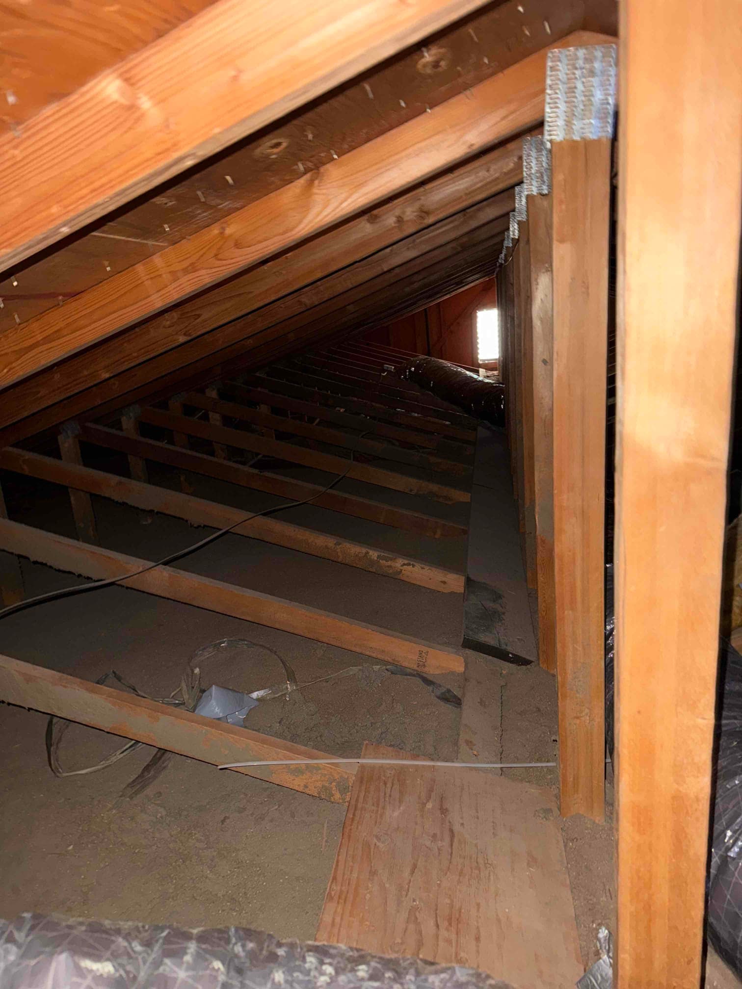 Flexible insulated duct runs through attic framing with loose boards and wiring visible.