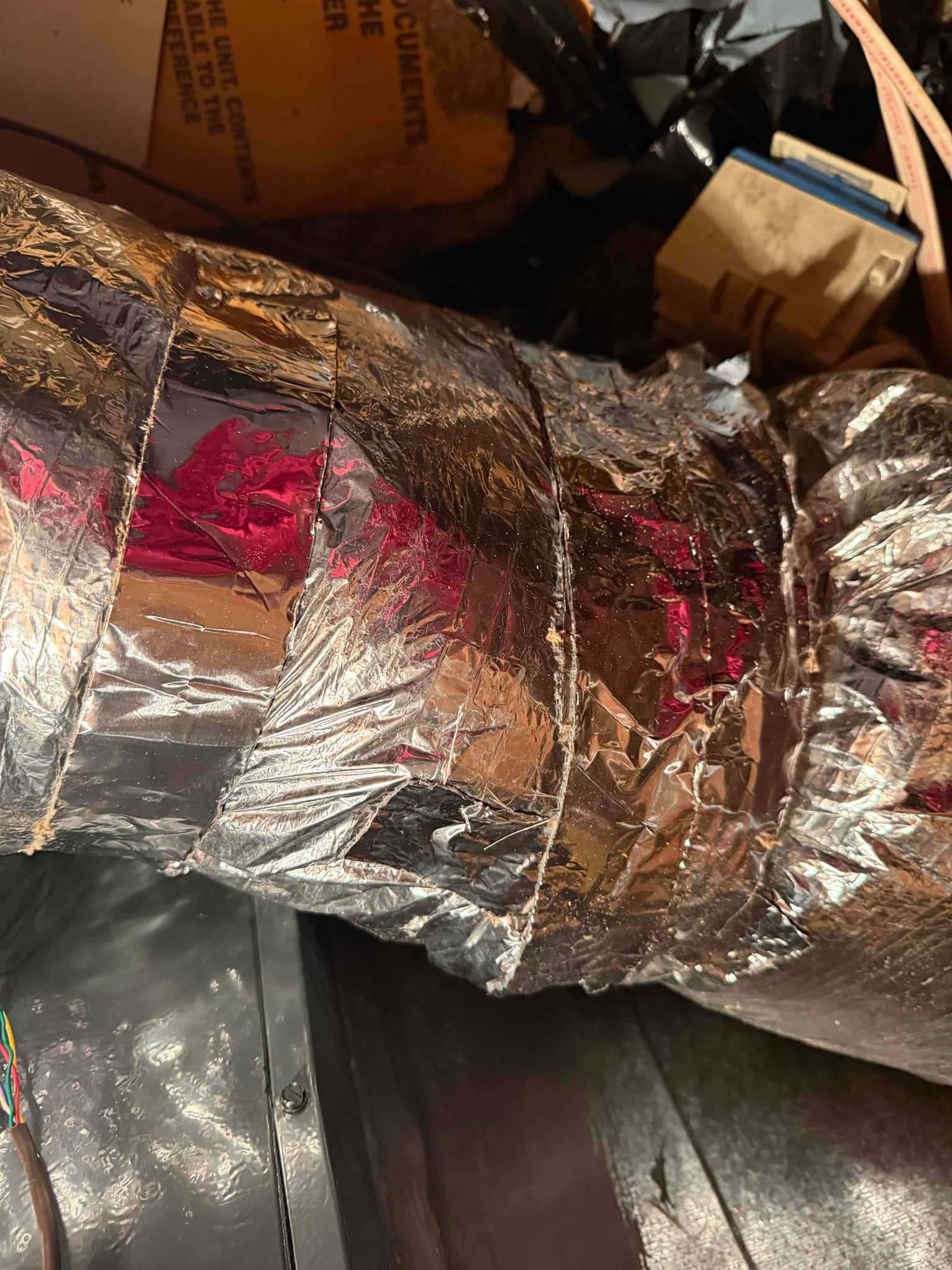 Foil-insulated flexible duct connected above the air handler cabinet, with multiple wraps of foil tape.