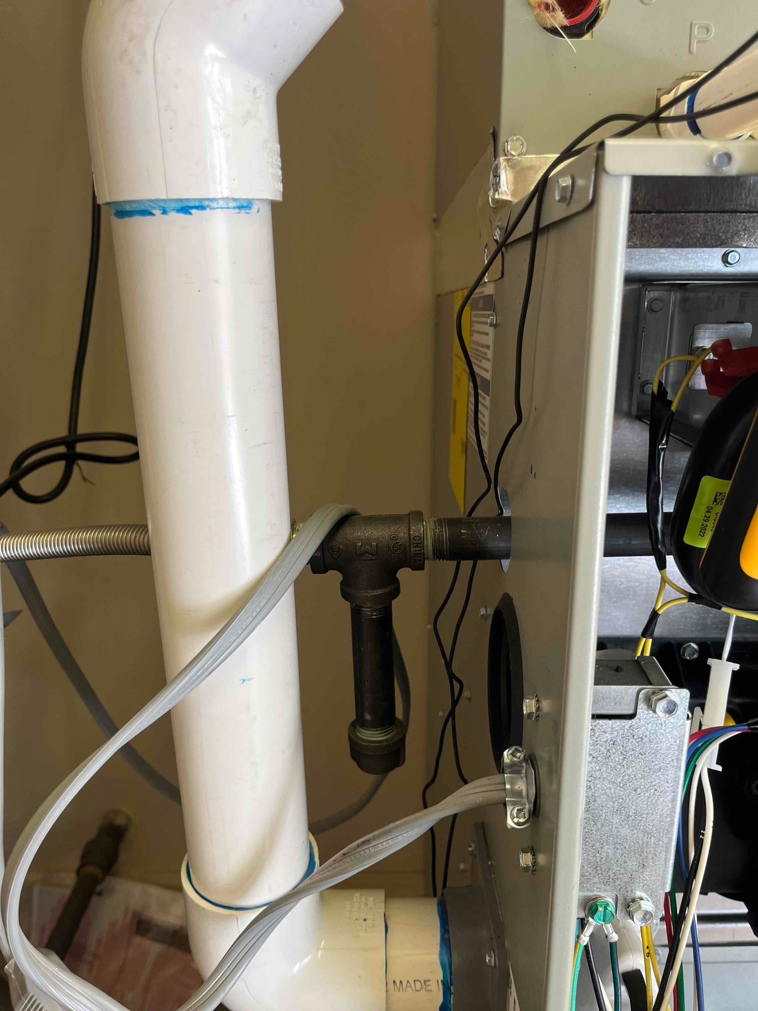 Furnace cabinet open beside PVC vent piping, showing black gas line with sediment trap and clear pressure switch tubing.