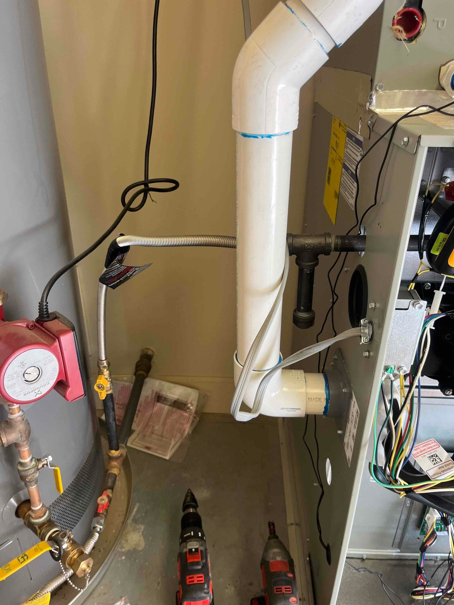 Furnace cabinet open showing PVC vent and condensate drain connections, wiring harness visible, with adjacent water heater and shutoff valves.