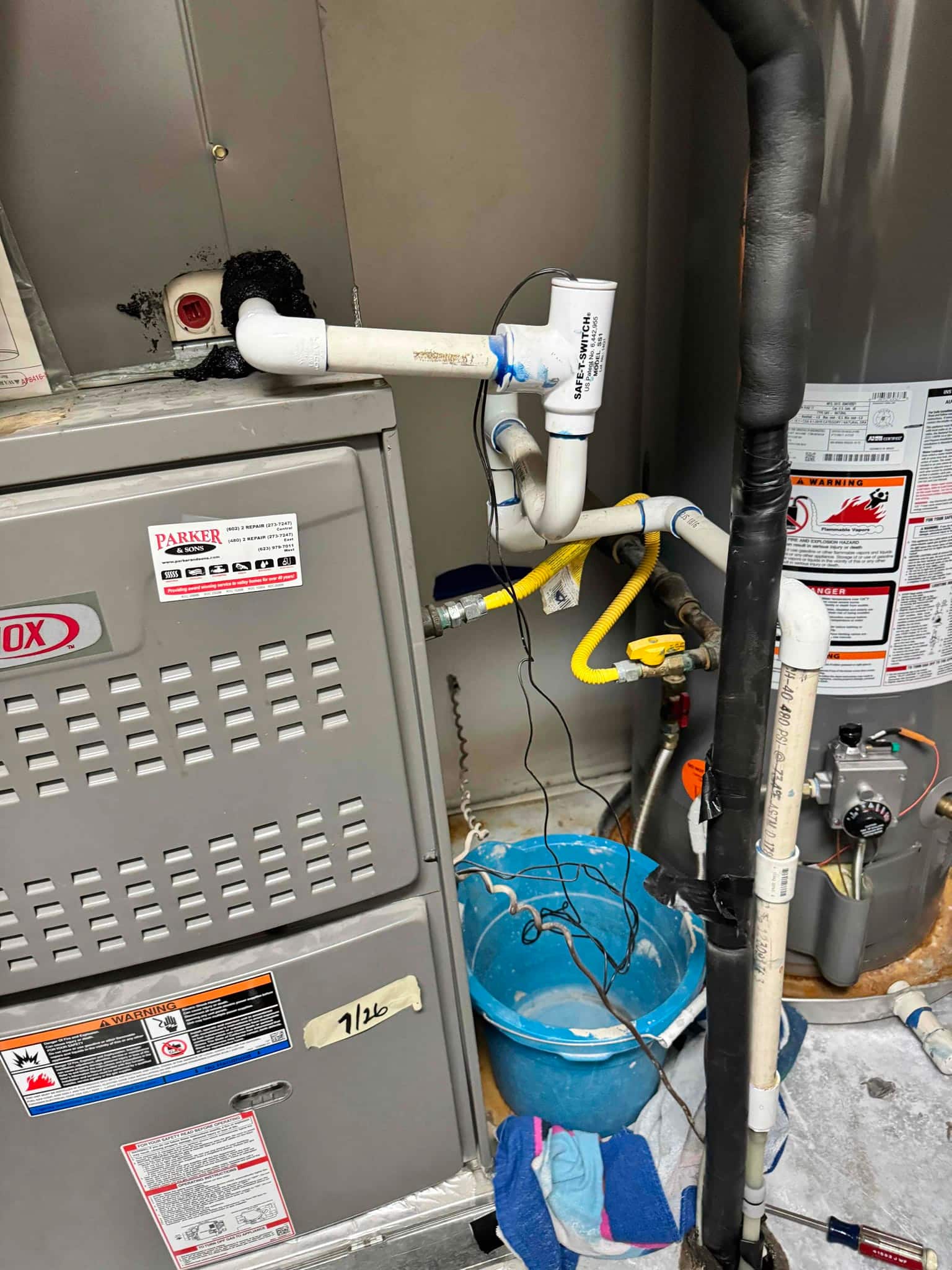 Furnace cabinet with PVC condensate drain and inline float switch, next to insulated refrigerant line and adjacent water heater.