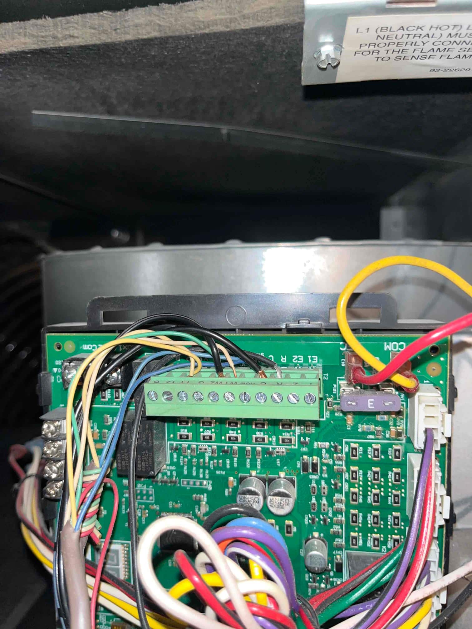 Furnace control board with multiple connected low-voltage and line-voltage wires, terminals, and a purple blade fuse.
