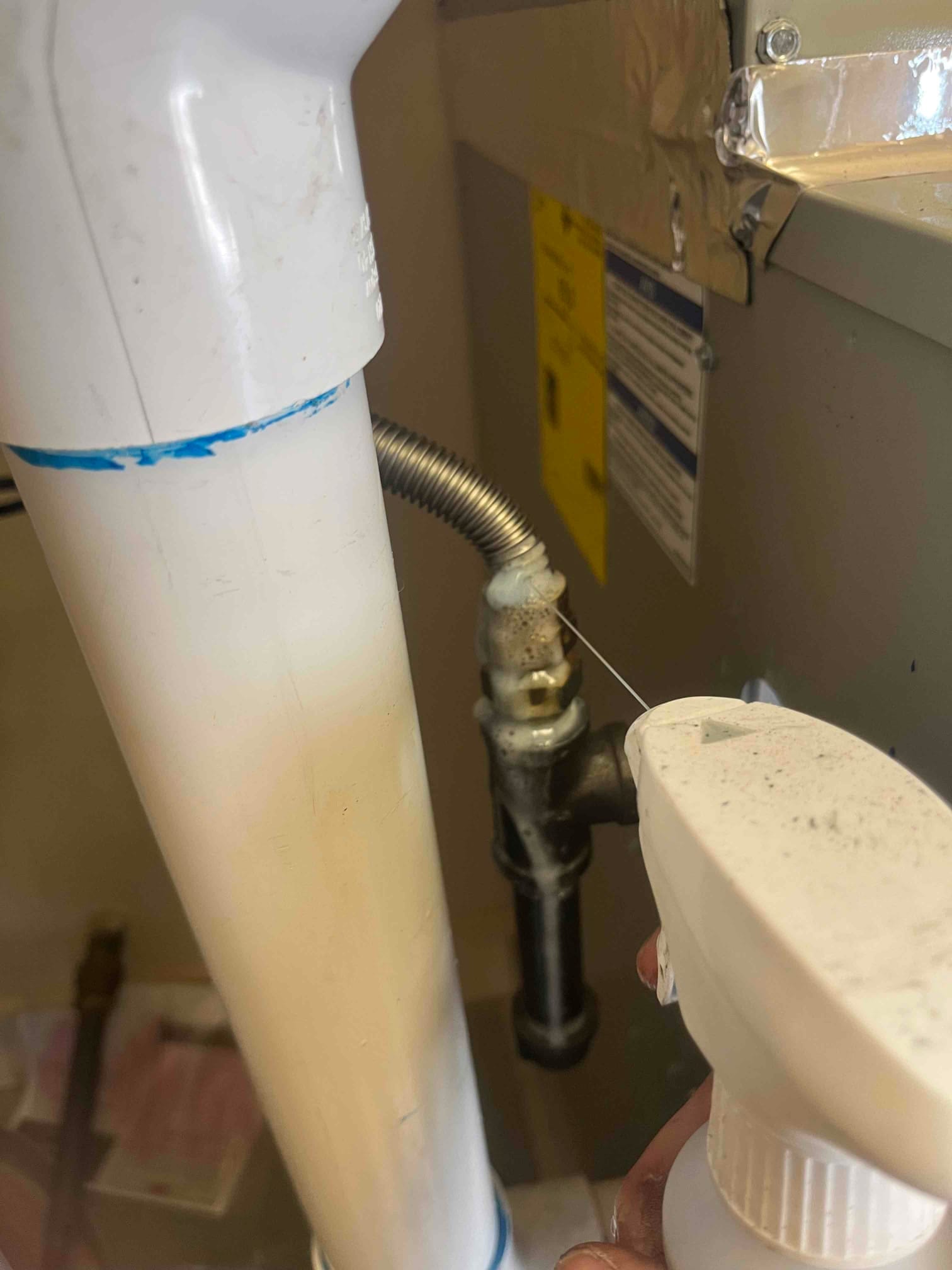 Gas line with sediment trap and flexible connector beside a PVC vent pipe near the furnace housing.