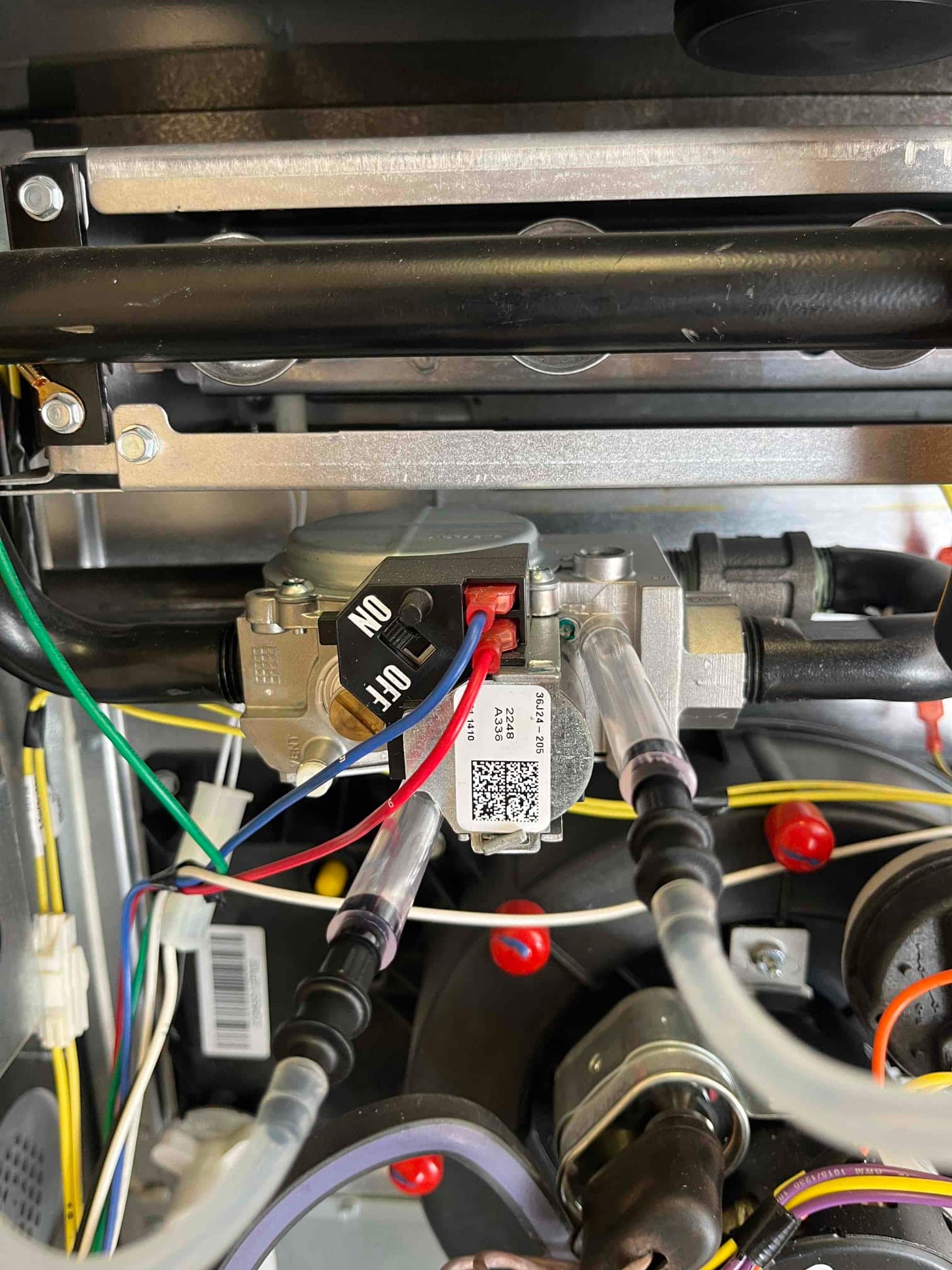 Gas valve with ON/OFF switch shown inside furnace cabinet, with connected wiring, pressure tubes, and nearby burner manifold.