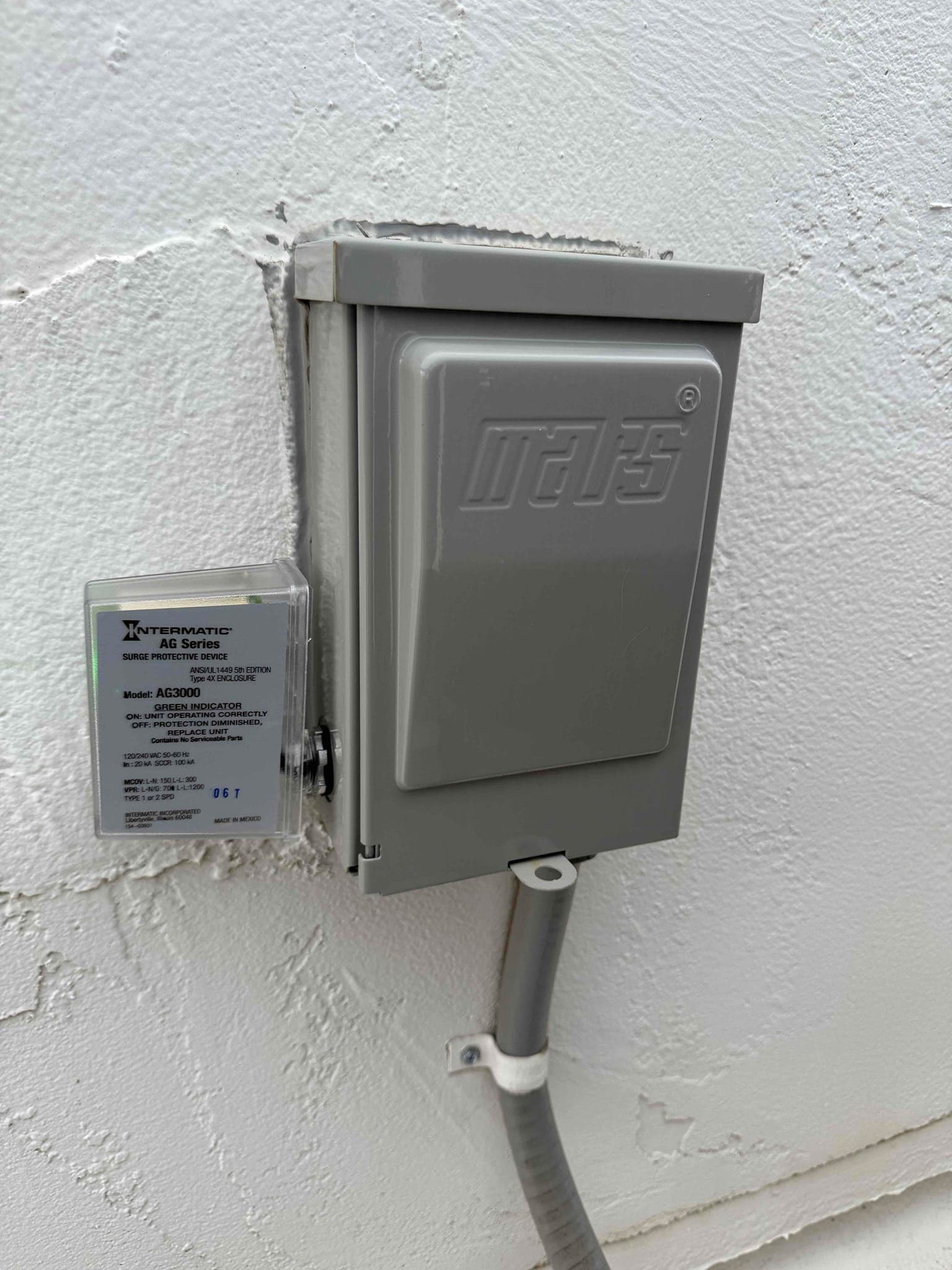 Gray outdoor electrical disconnect enclosure with adjacent surge protective device and flexible conduit secured to the exterior wall.