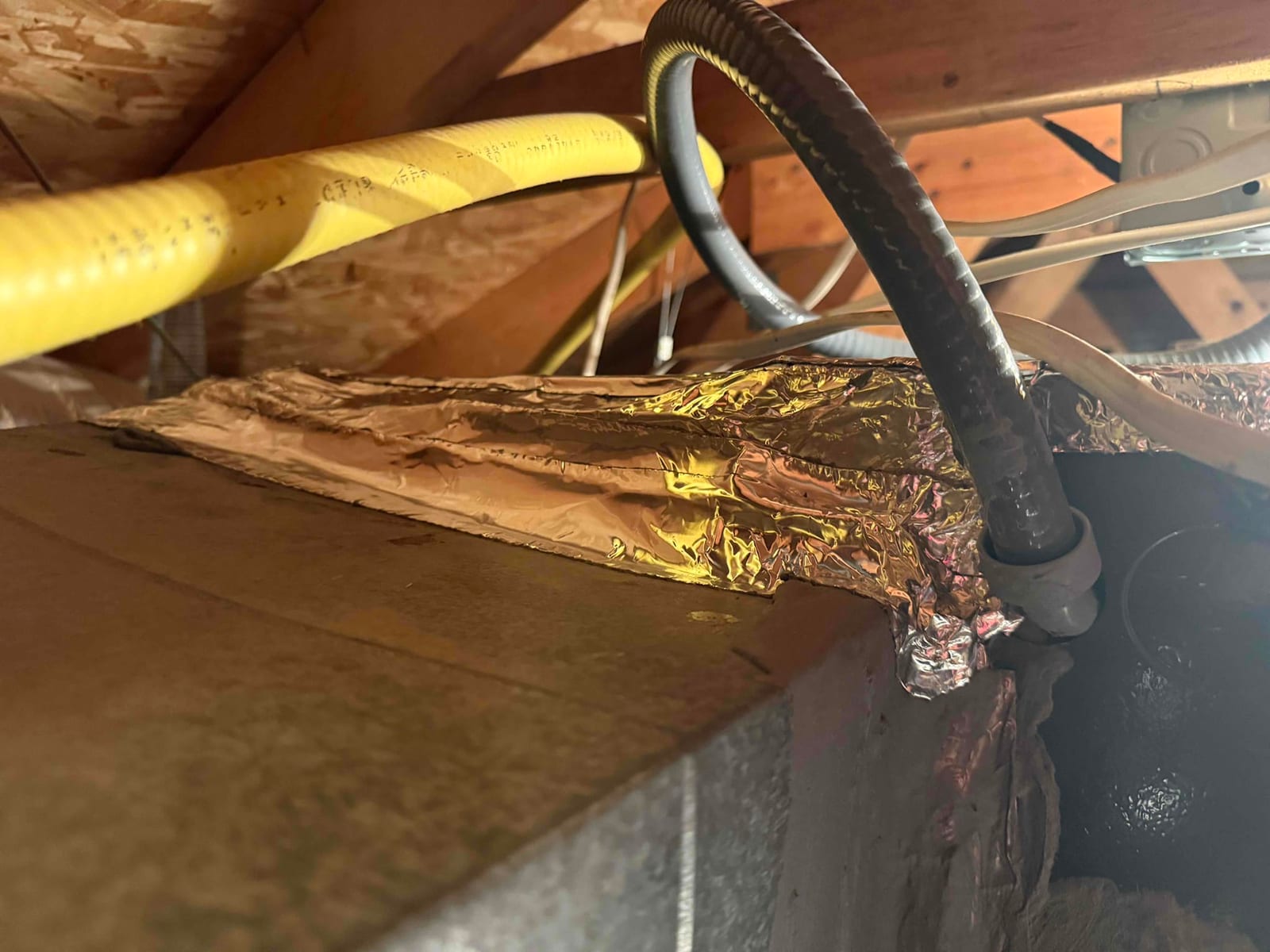 HVAC cabinet in attic with foil tape along a top seam and flexible electrical conduit entering.