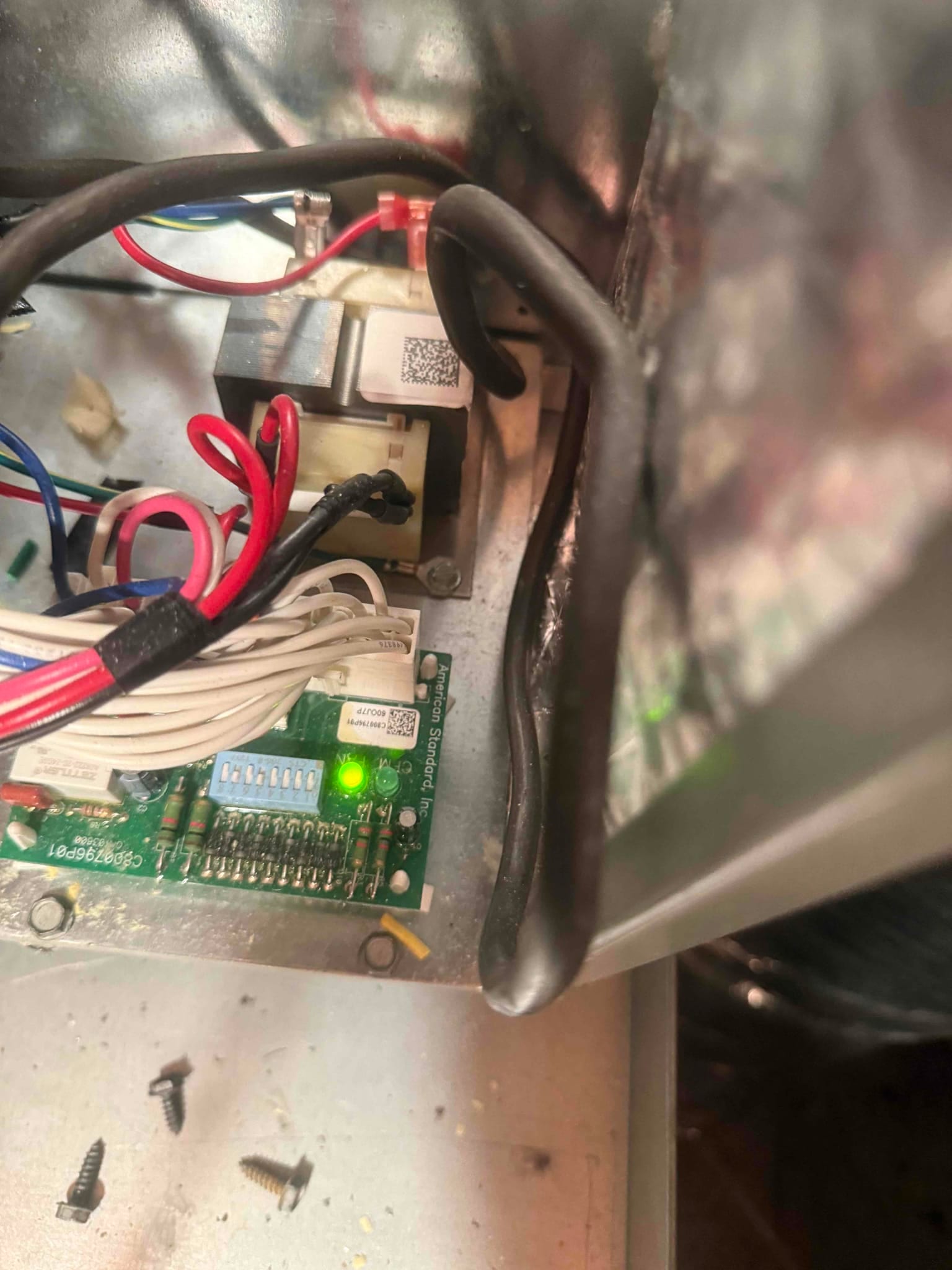 HVAC control board with DIP switches, green status LED, transformer, and multiple wires inside the equipment cabinet.