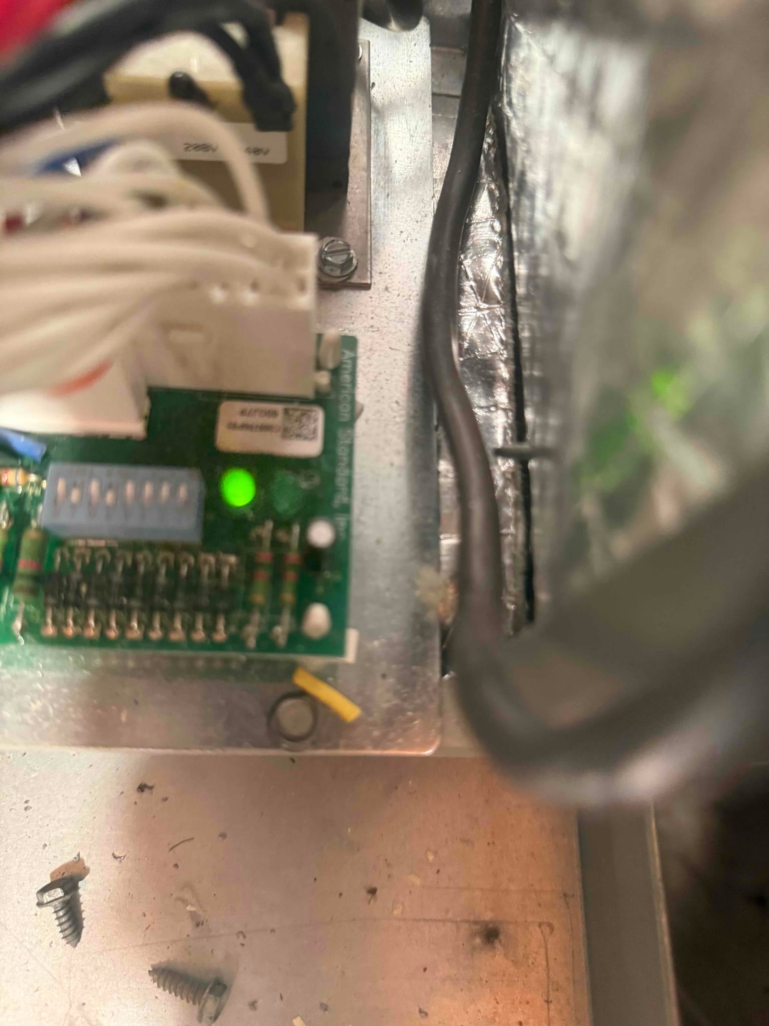 HVAC control board with wired connector, DIP switch block, and green status LED illuminated inside air handler.