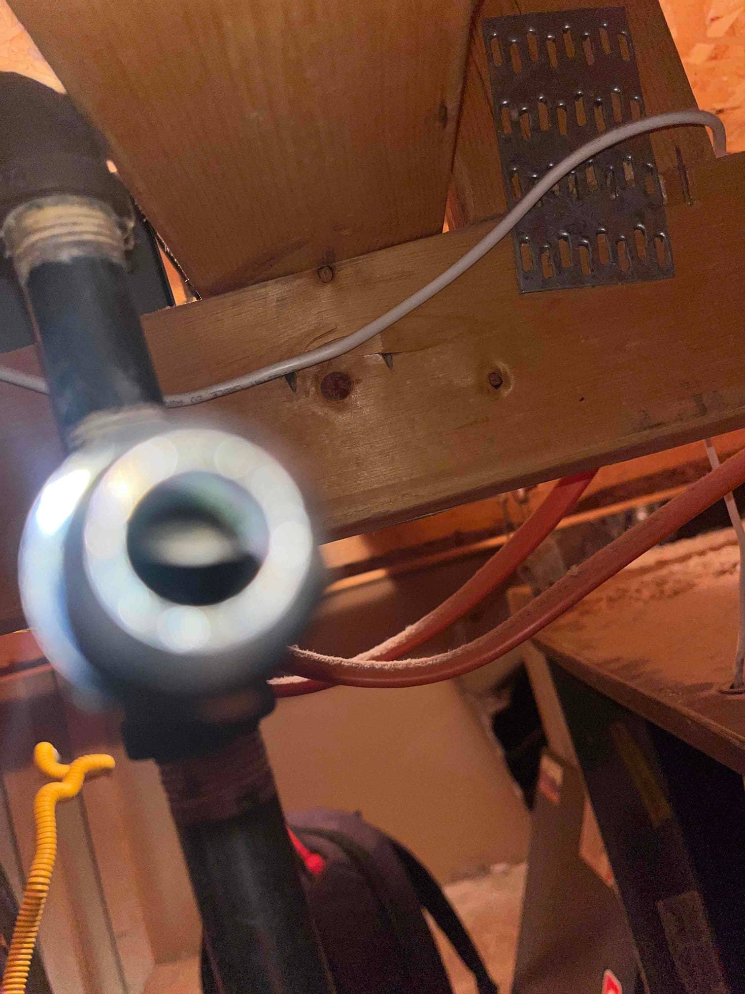 HVAC equipment cabinet in attic with nearby wiring, flex gas connector, and insulated tubing and piping beneath a floor joist.