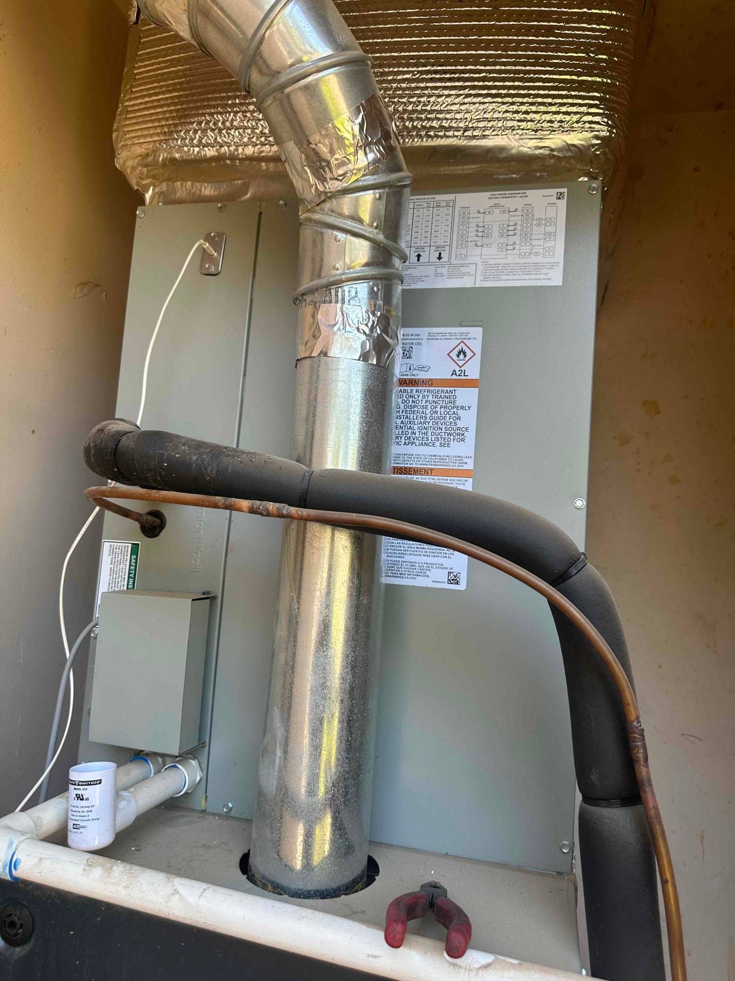 Indoor air handler with galvanized flue, insulated refrigerant lines, PVC condensate drain, and access panel labels visible.