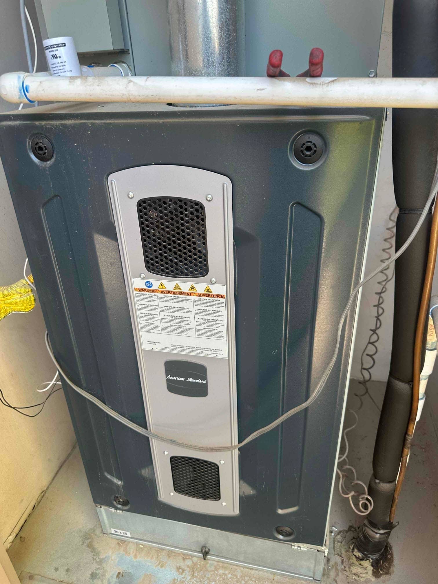 Indoor furnace cabinet with front panels, condensate drain piping, and insulated refrigerant lines visible at the side.