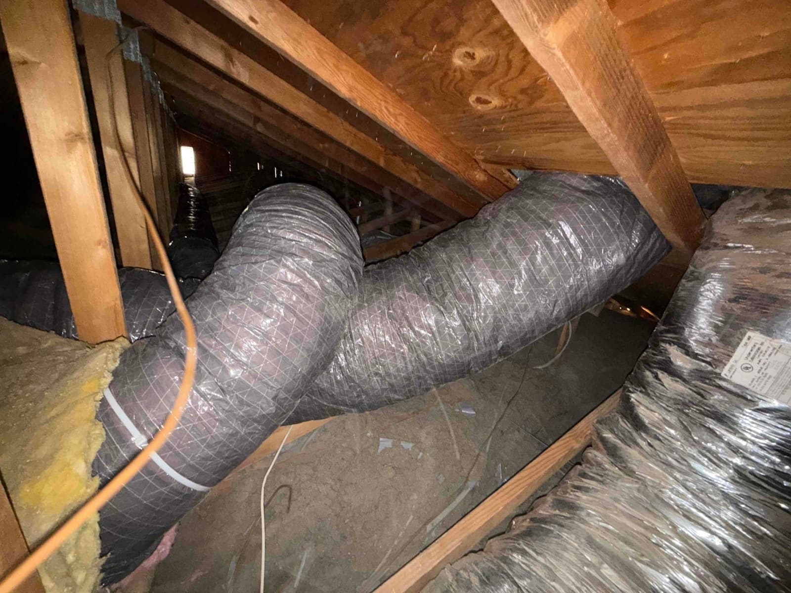 Insulated flexible HVAC ducts run through the attic bay between rafters, with a tight bend and plastic support strap visible.