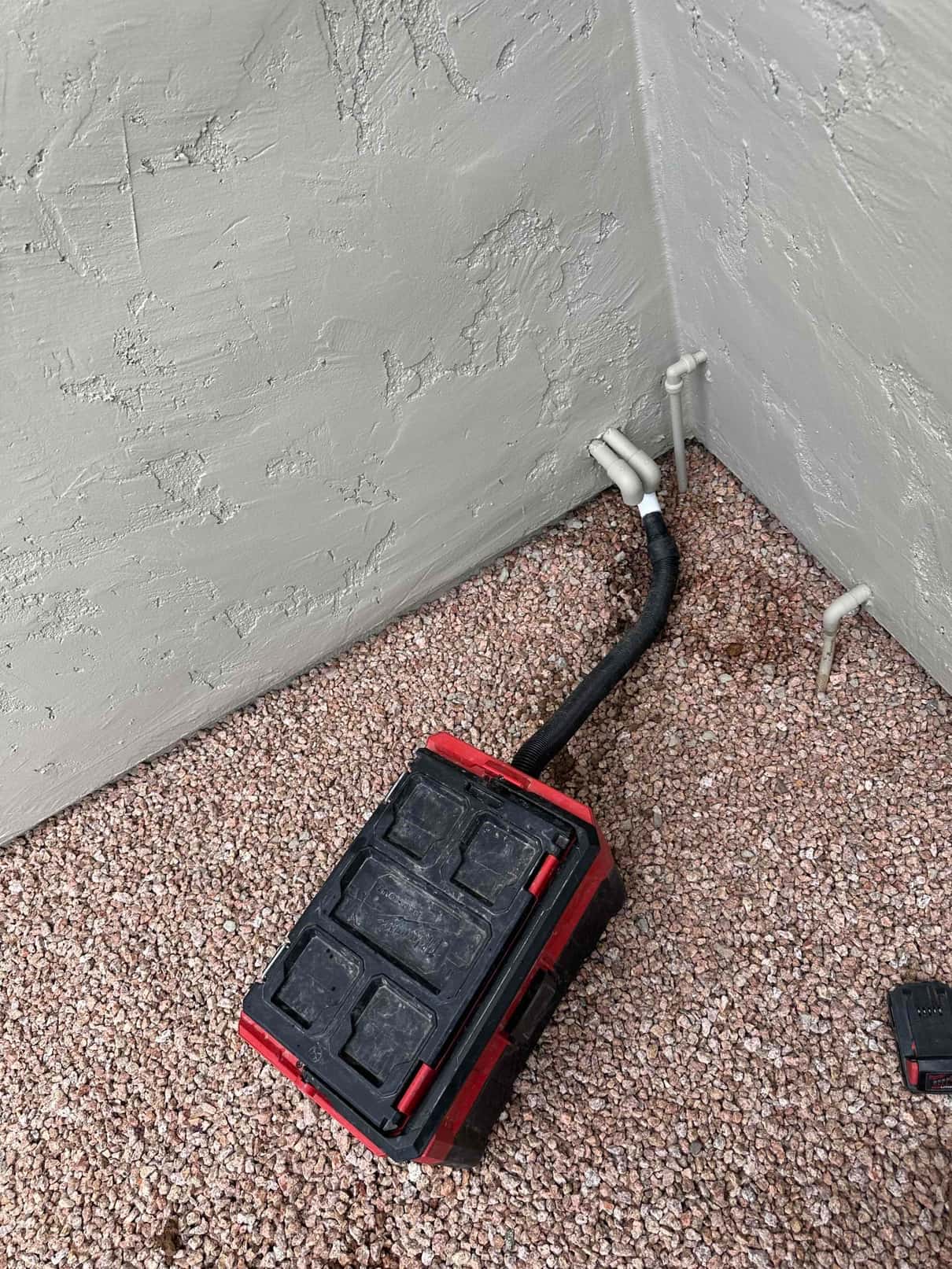 Insulated refrigerant line and two PVC condensate drain outlets exit an exterior stucco wall above gravel.