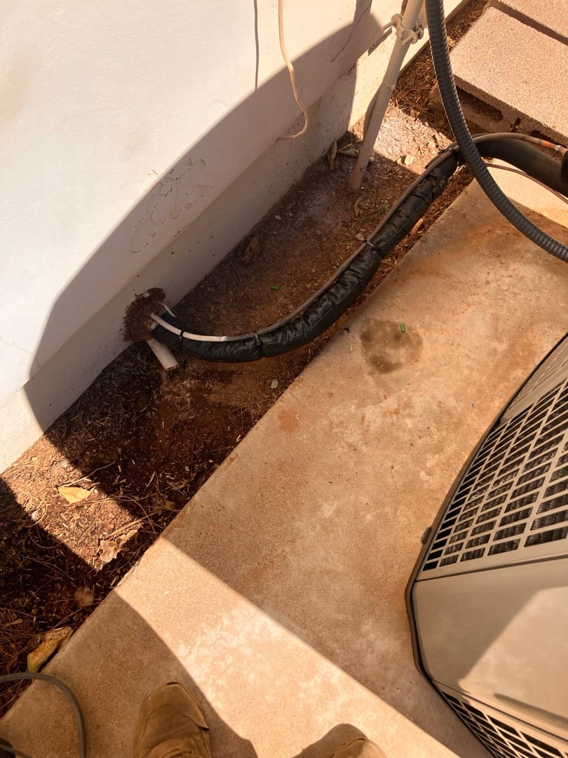 Insulated refrigerant line set and condensate drain exit the wall and route to the outdoor condenser on a level pad.
