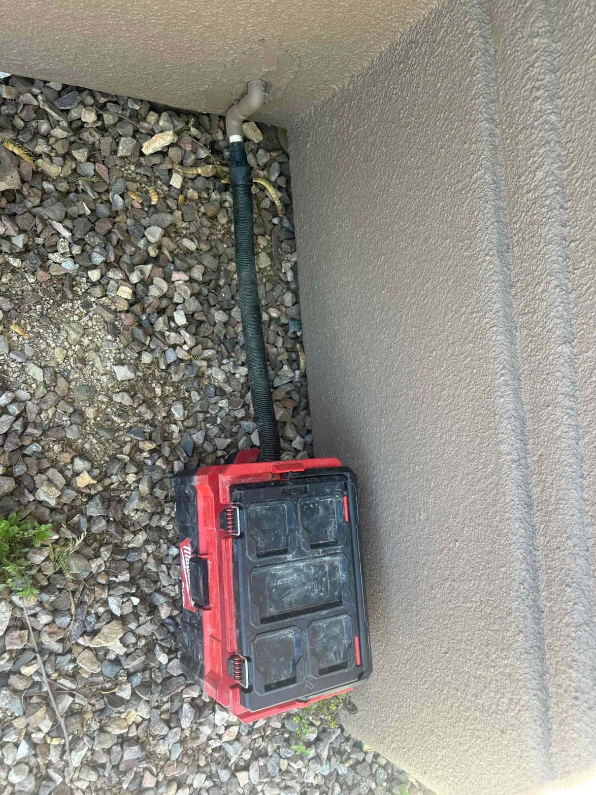 Insulated refrigerant line set exits exterior stucco wall through elbow fitting above gravel.
