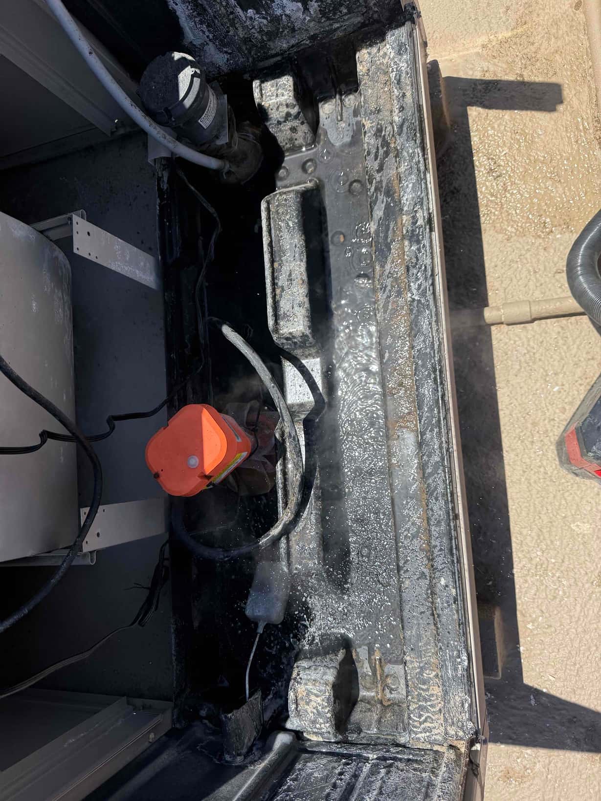 Interior base pan of an HVAC cabinet with water residue, wiring, and components visible during inspection.