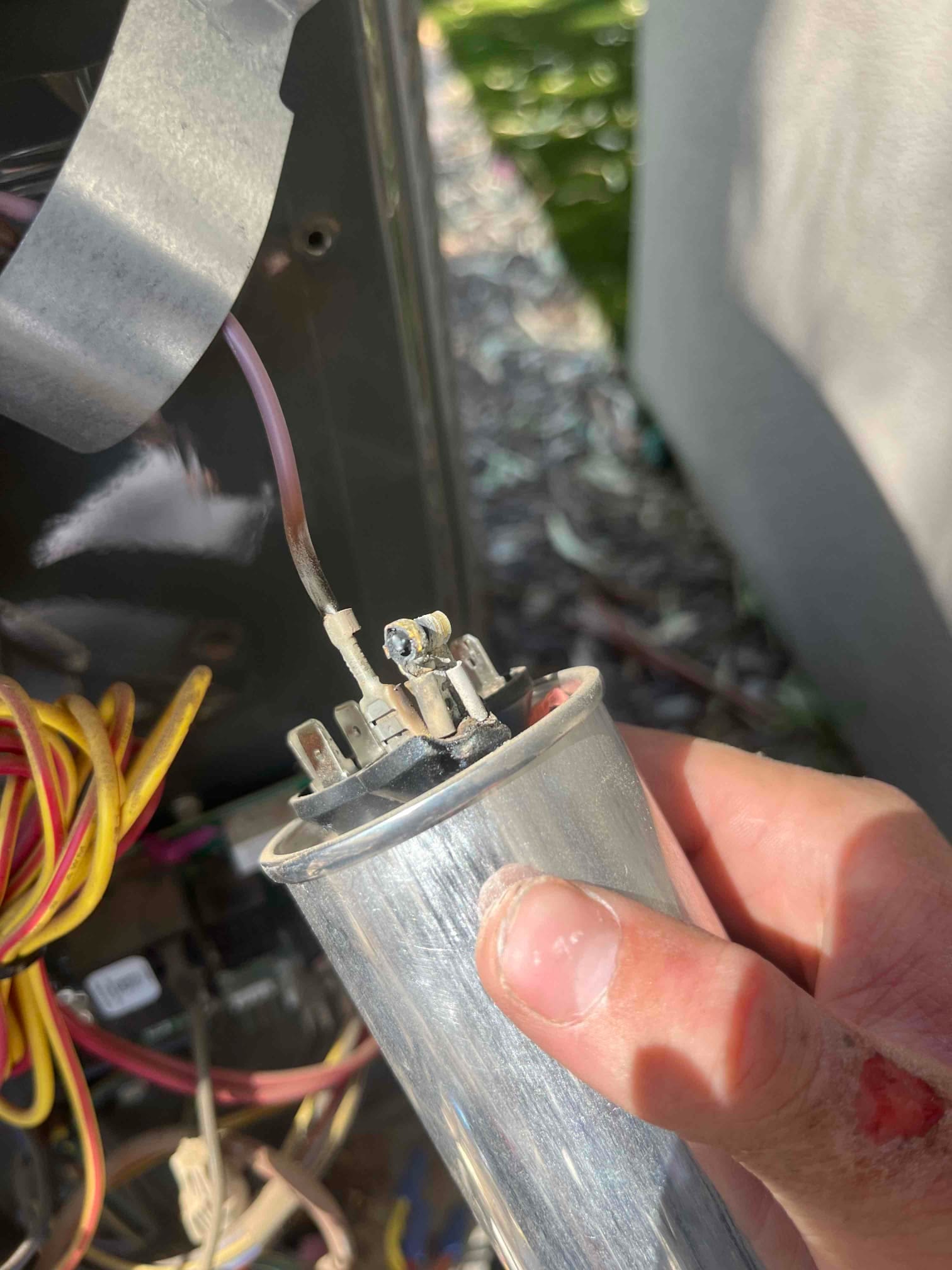 Metal can capacitor held near the condenser compartment, with a disconnected wire and dark discoloration at one terminal.