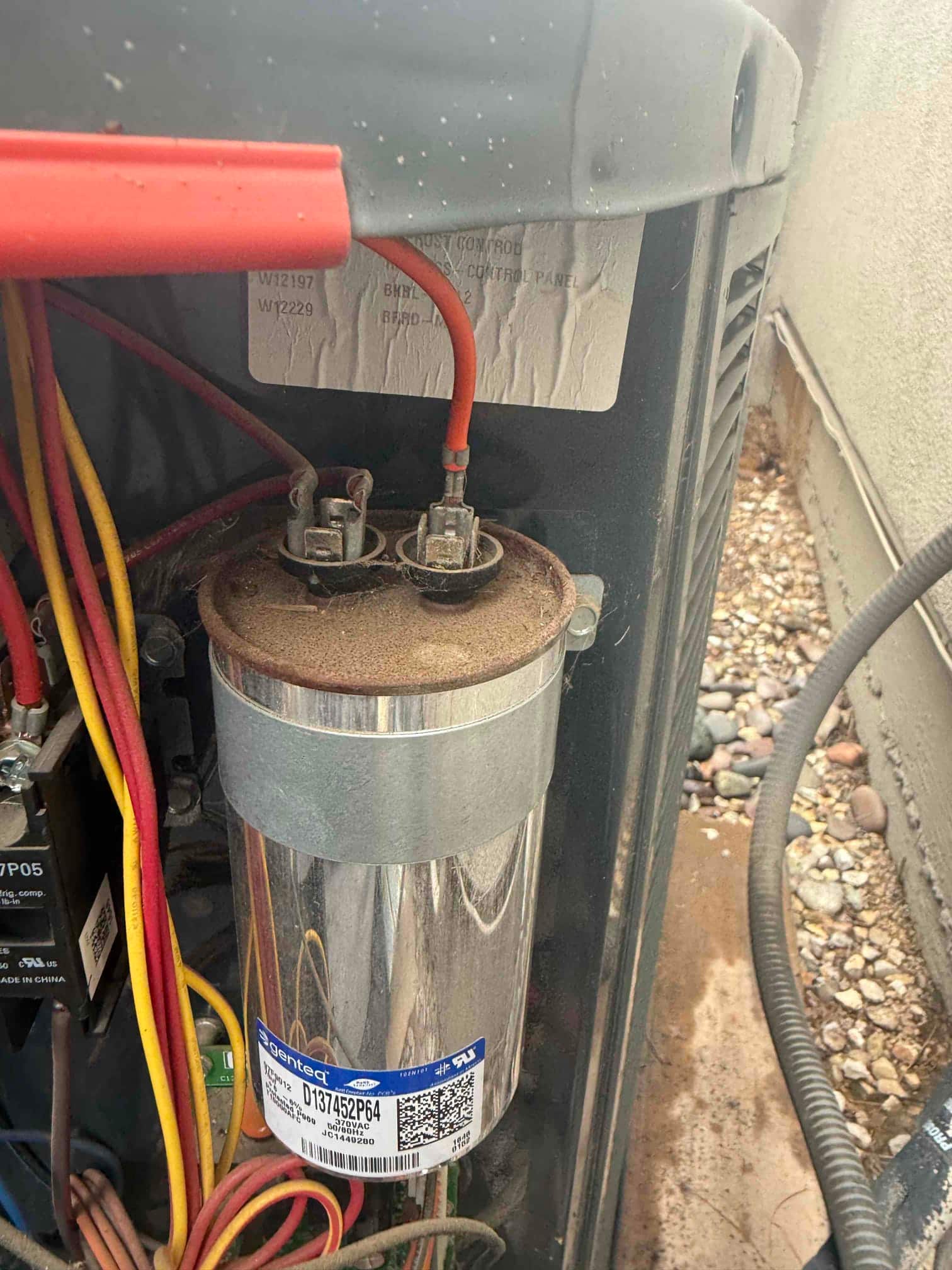 Metal can capacitor in the outdoor condenser compartment with connected red and yellow wires and nearby contactor.