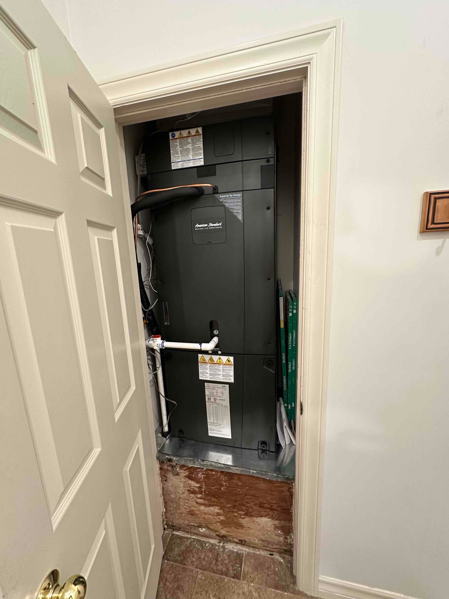 New air handler installed in a closet with insulated refrigerant lines and PVC condensate drain connected on a metal base.