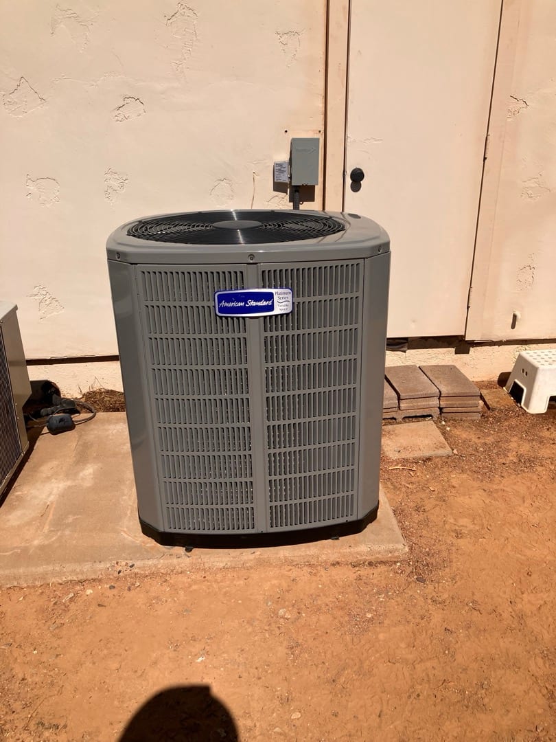 New outdoor condenser set on a level pad with nearby electrical disconnect mounted on the wall.