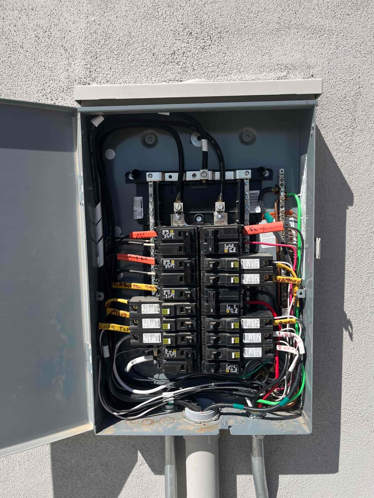 Open electrical breaker panel showing multiple breakers, labeled circuit wires, grounding and neutral bars, and service conductors.