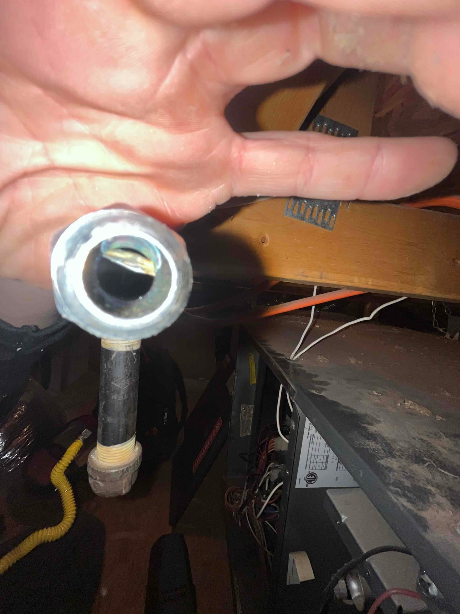 Open gas pipe with threaded connection held near a furnace cabinet with wiring exposed.
