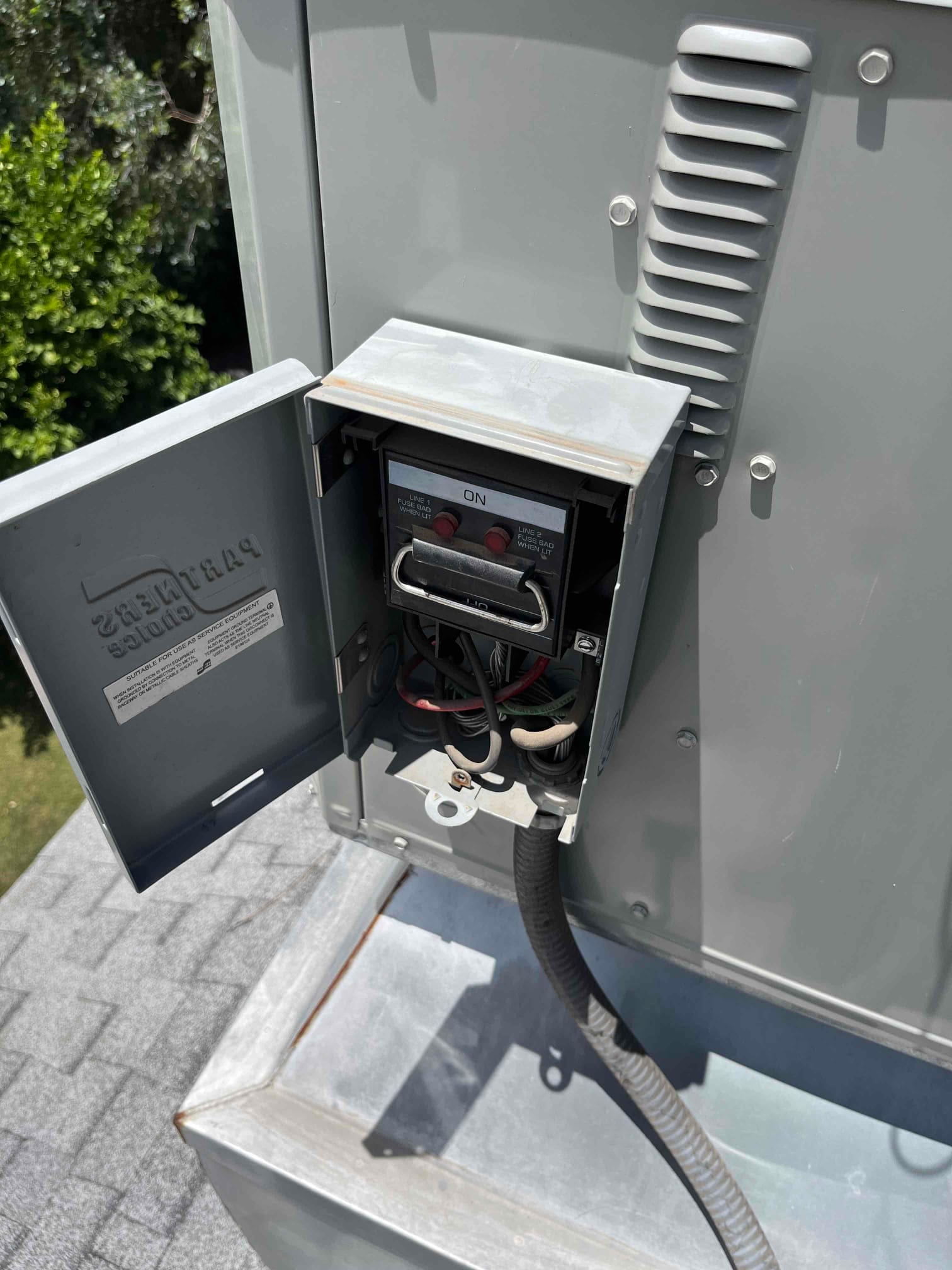 Open outdoor HVAC disconnect shows a pull-out handle marked ON, with internal wiring and flexible conduit entering the bottom of the box.