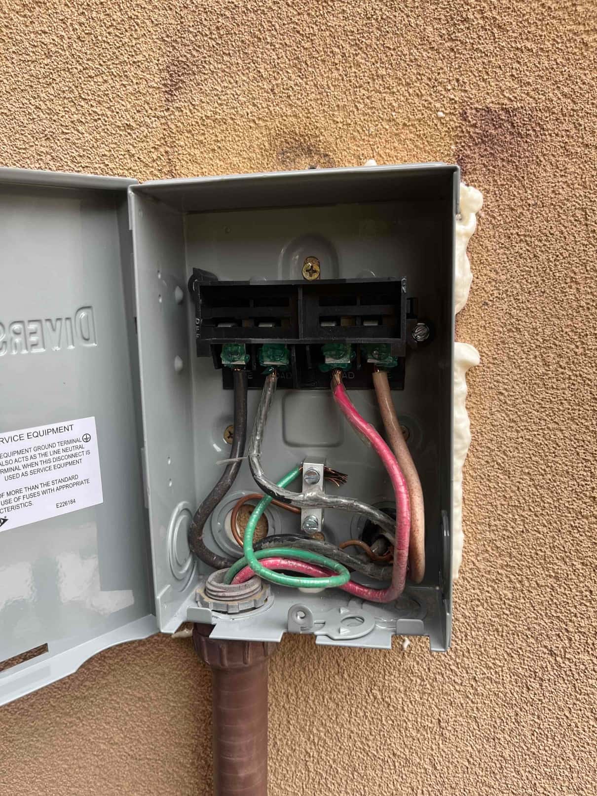 Open outdoor service disconnect shows multiple conductors routed to the terminal block, with one wire end exposing copper strands.