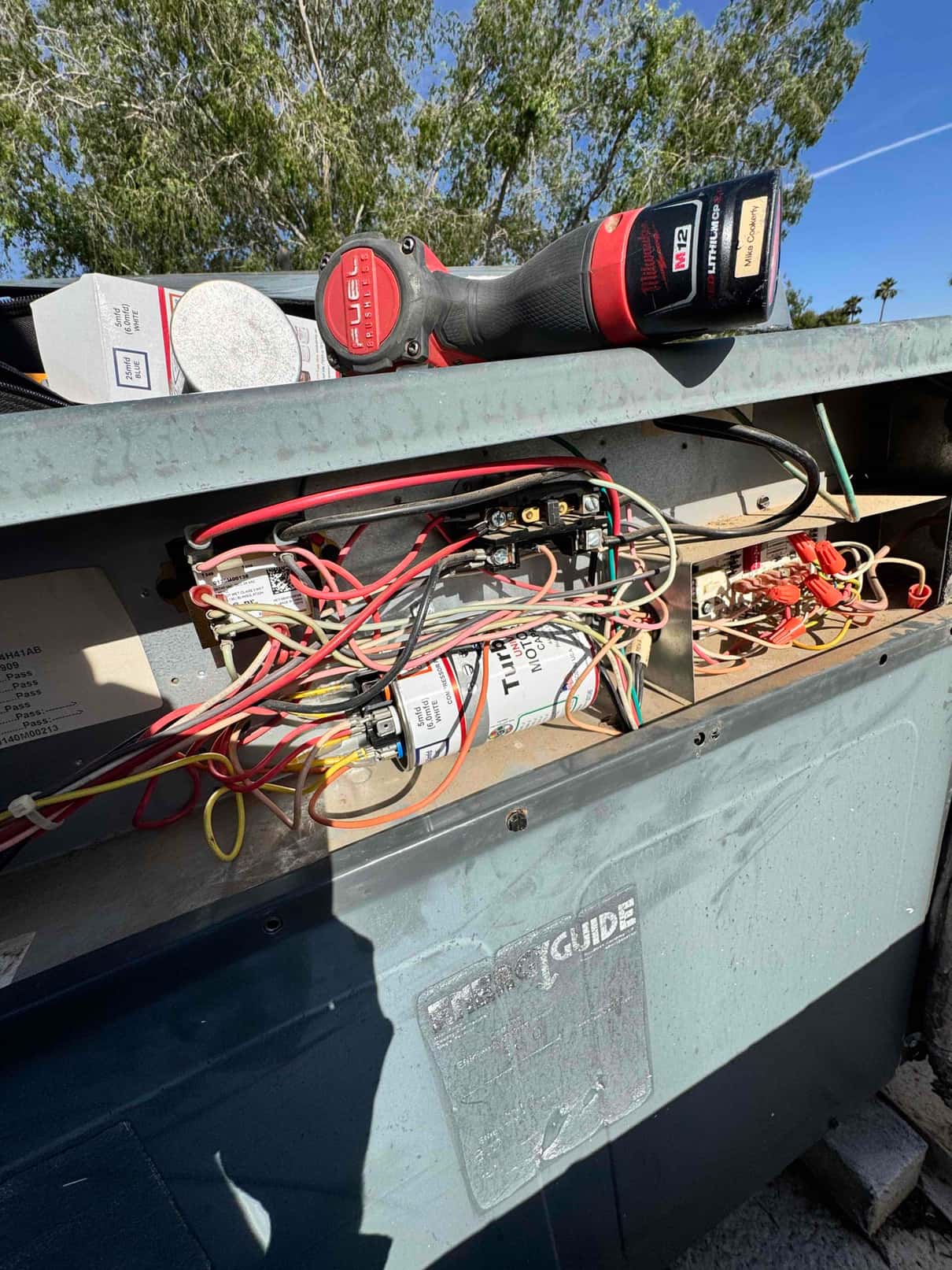 Open outdoor unit control compartment showing wiring, contactor, and an aluminum run capacitor with connected leads and terminal cover.