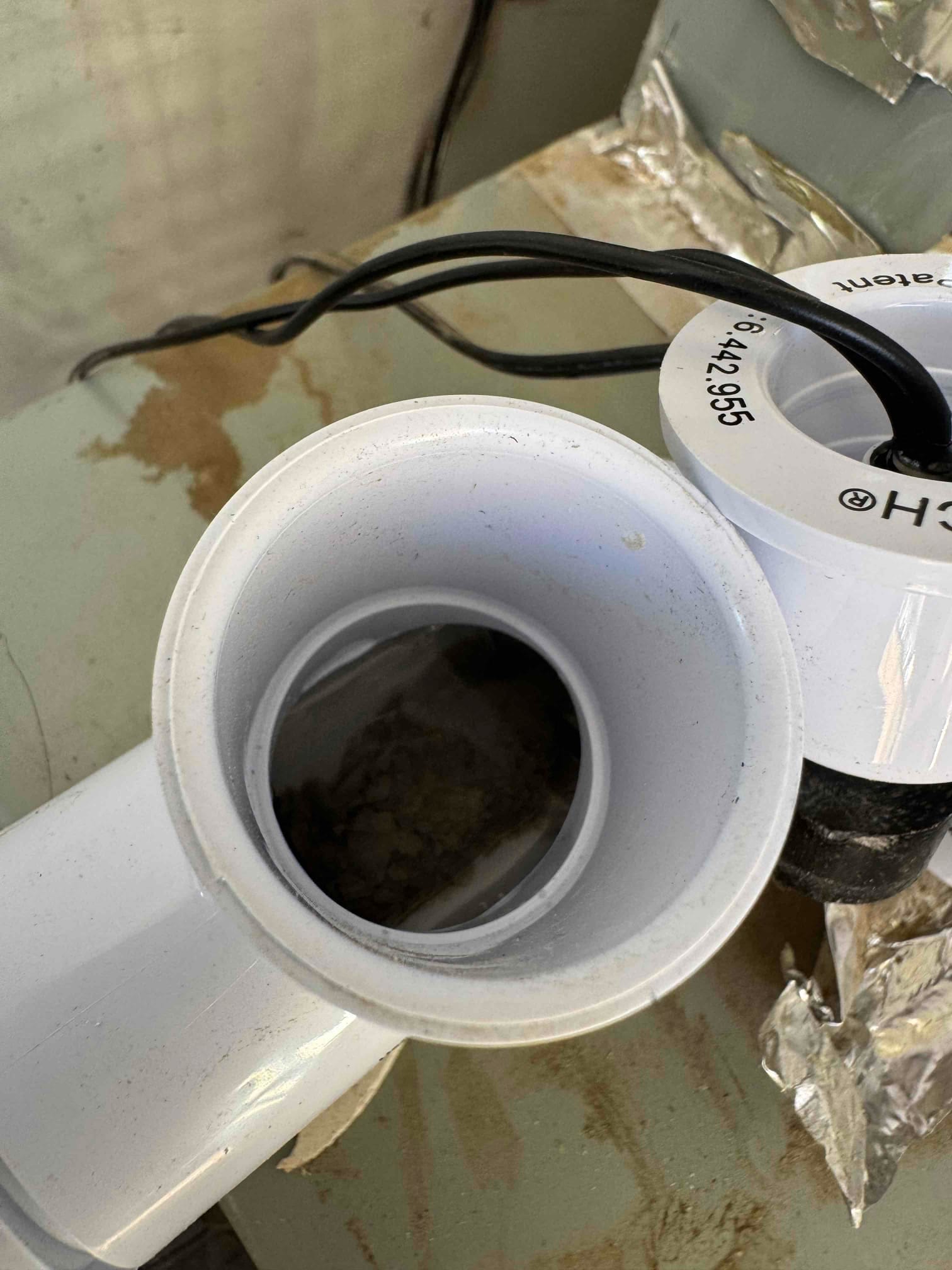 Open PVC condensate drain cleanouts on the equipment cabinet, with standing water and debris visible inside.