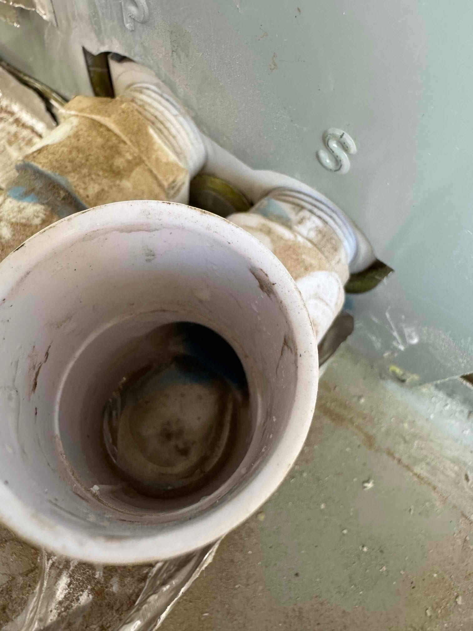 Open PVC pipe beside two threaded PVC fittings entering the equipment cabinet, with moisture and residue visible around the opening.