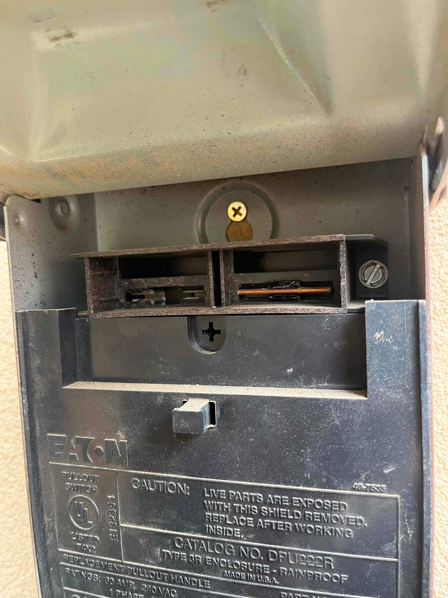 Outdoor AC disconnect with pullout removed, showing contact slots and embossed safety labeling on the cover.