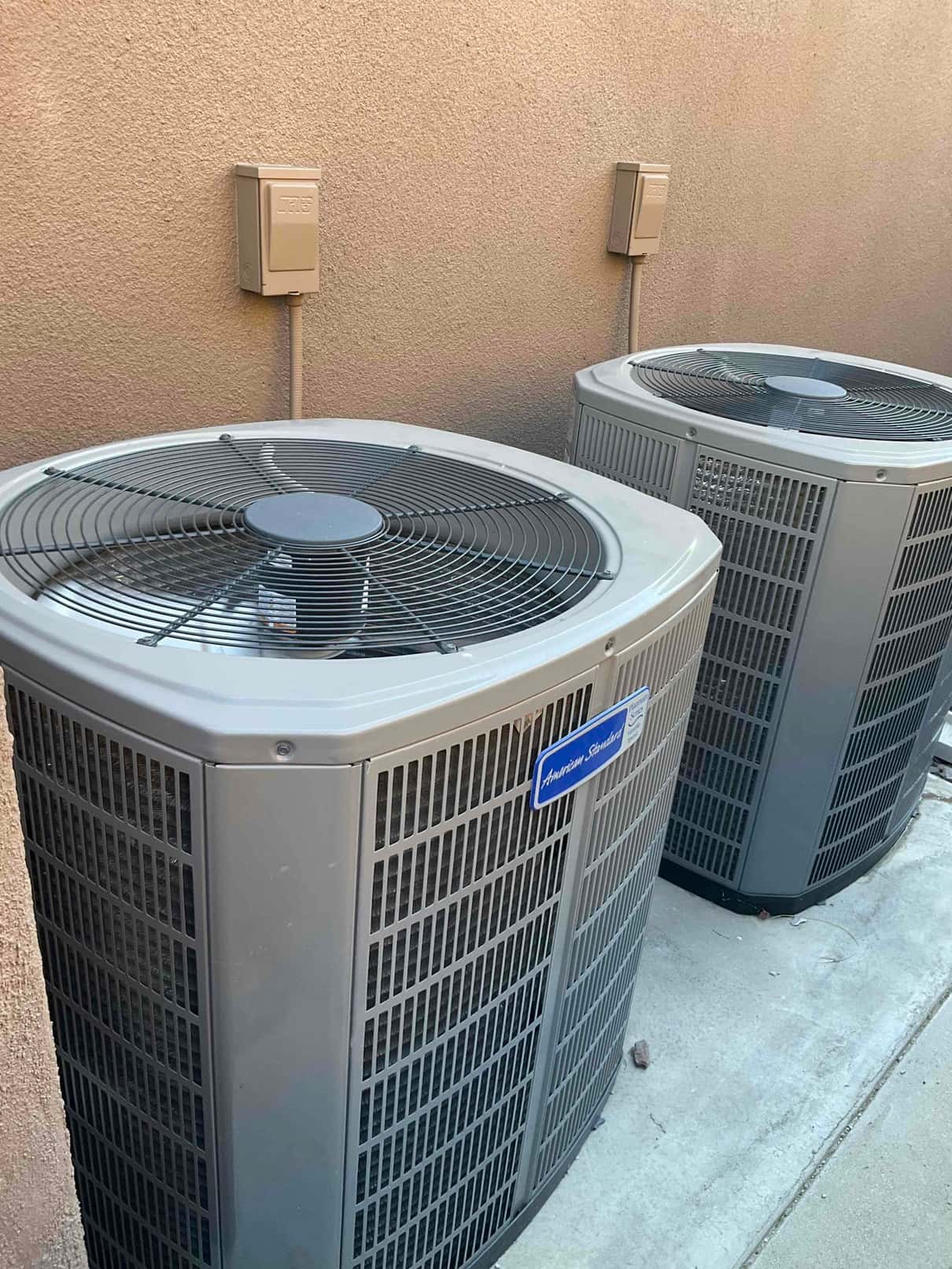 Two outdoor air-conditioning condenser units sit beside the exterior wall, with electrical service disconnects mounted above each.