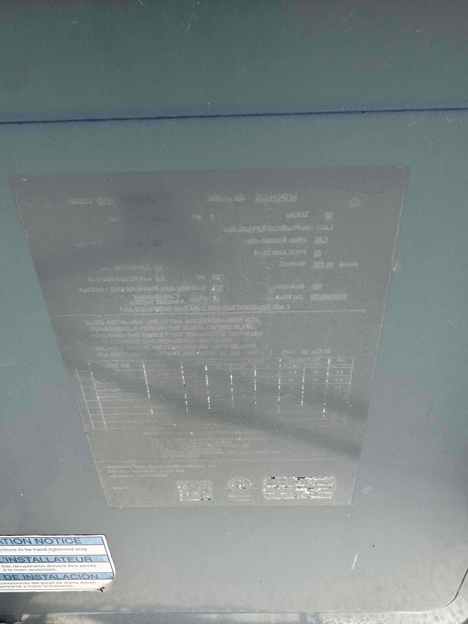 Outdoor condenser cabinet panel with a faded equipment label and instruction sticker, text not legible due to glare.
