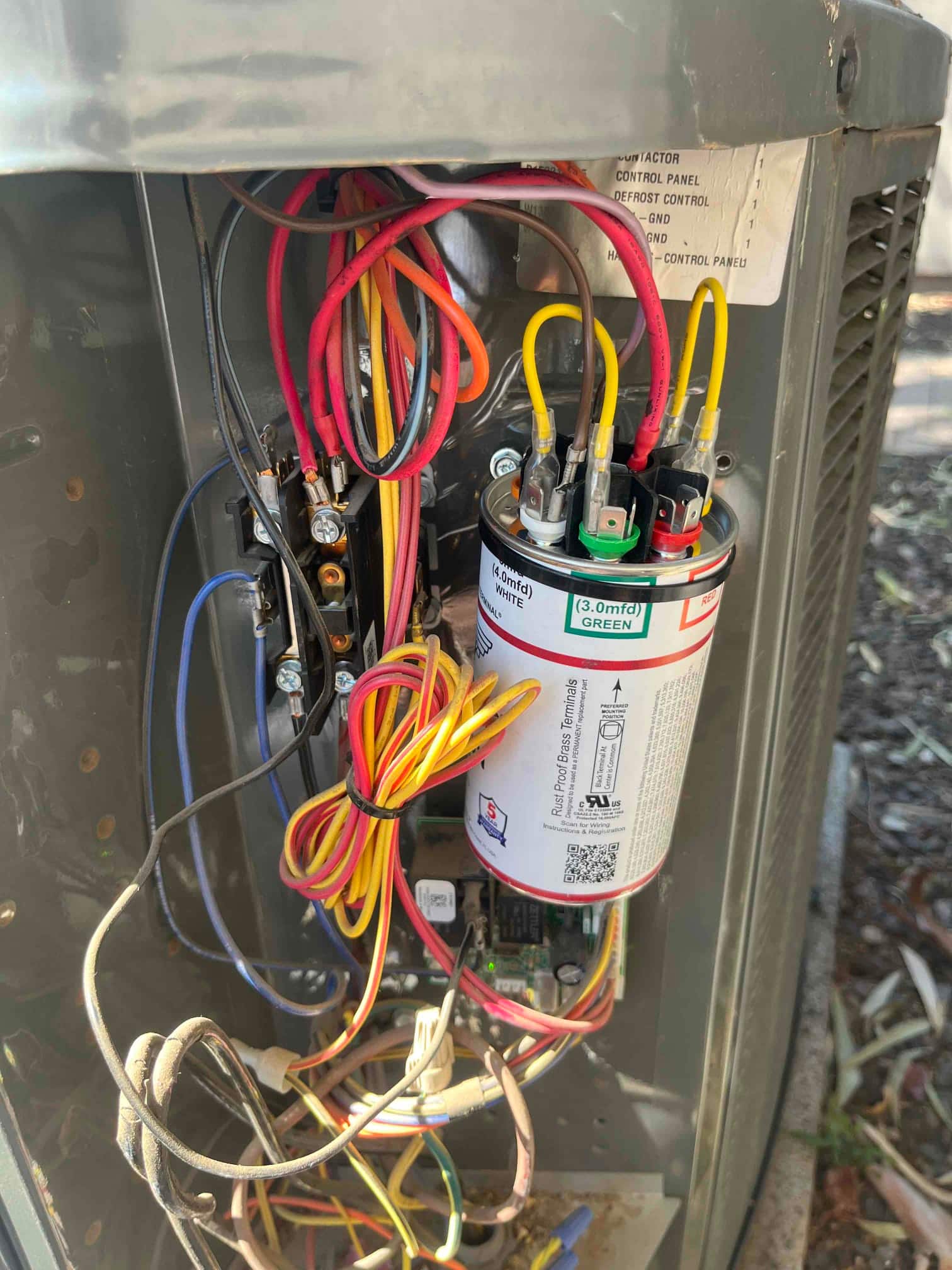 Outdoor condenser control panel showing a run capacitor labeled '(4.0 mfd) WHITE' and '(3.0 mfd) GREEN' with connected wiring.