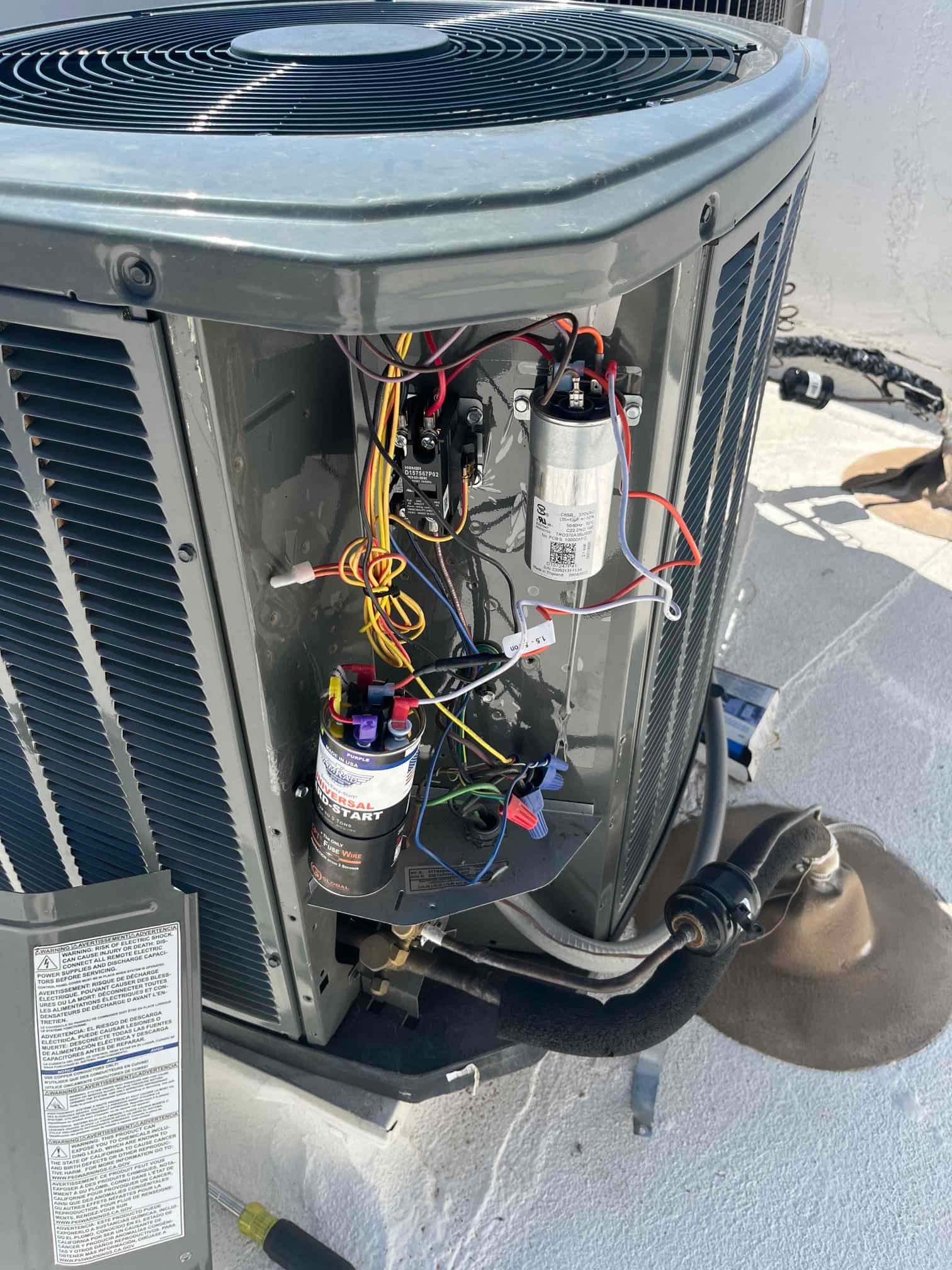 Outdoor condenser with service panel open, showing contactor, run capacitor, and hard-start kit wiring inside the control section.