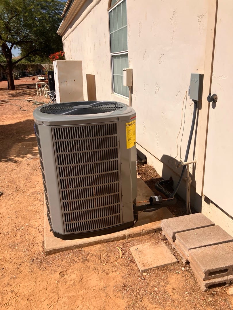 Outdoor condenser set on a level pad with insulated refrigerant lines and electrical disconnect mounted on the wall.