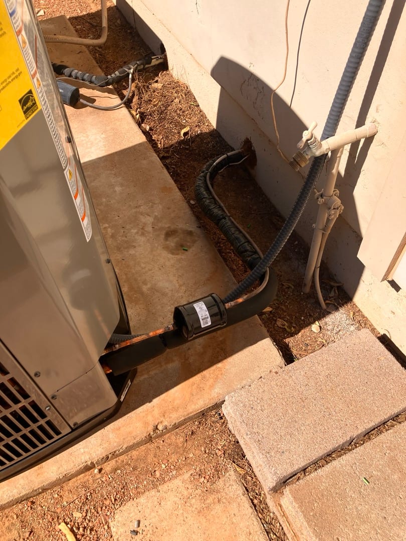 Outdoor condenser set on a pad with insulated refrigerant lines routed to the wall penetration and electrical conduit nearby.