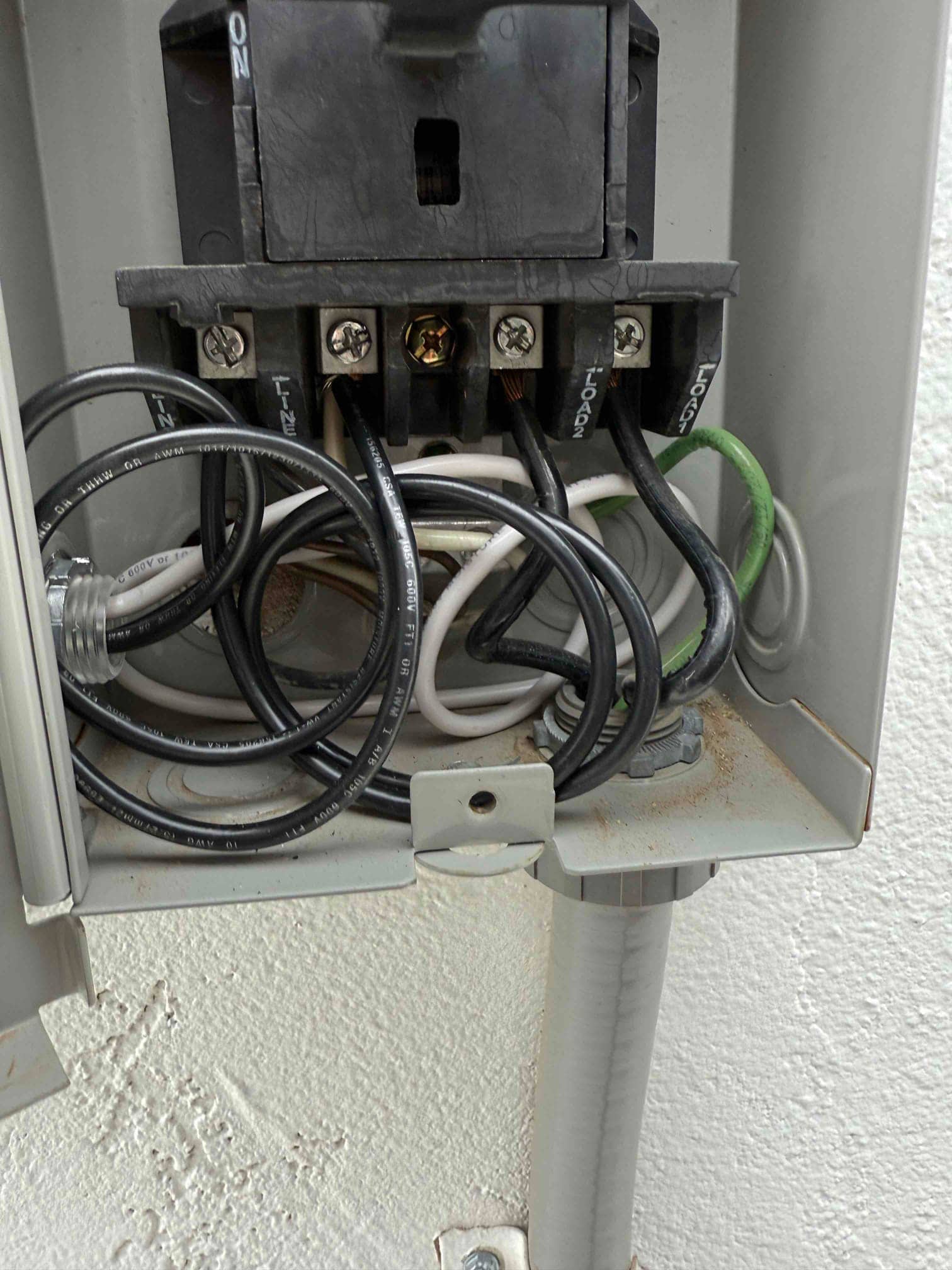 Outdoor disconnect box with pull-out switch and connected line, load, neutral, and ground conductors in conduit.
