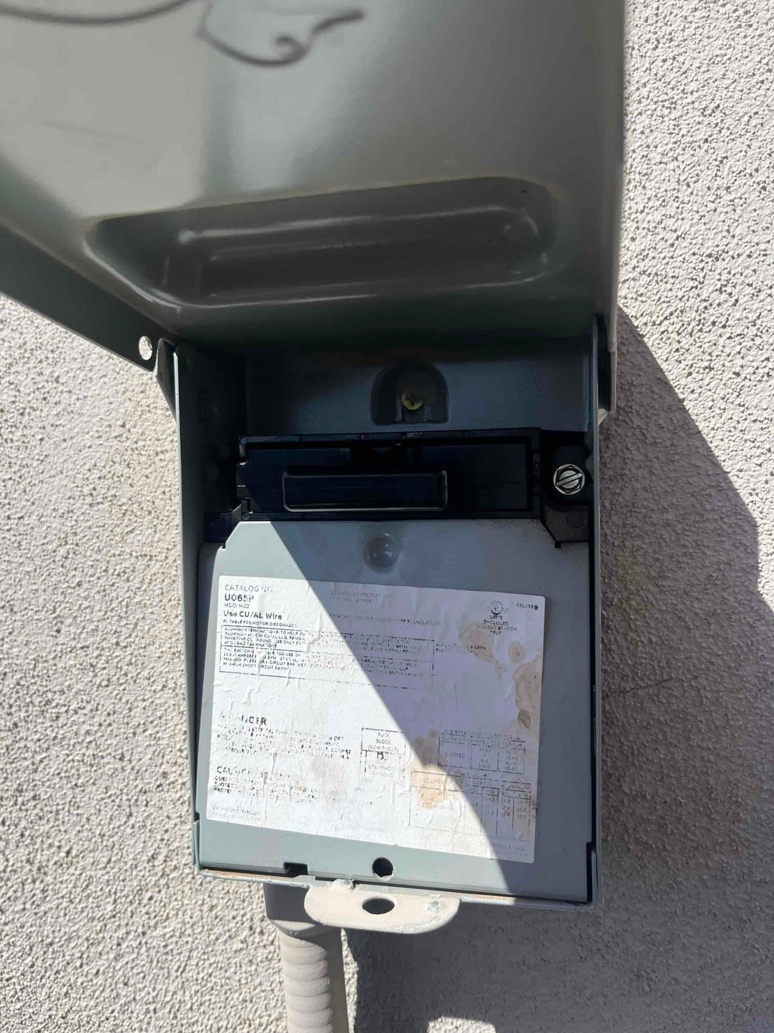 Outdoor electrical disconnect with cover open, showing pull-out handle, interior compartment, and a printed wiring label on the enclosure.