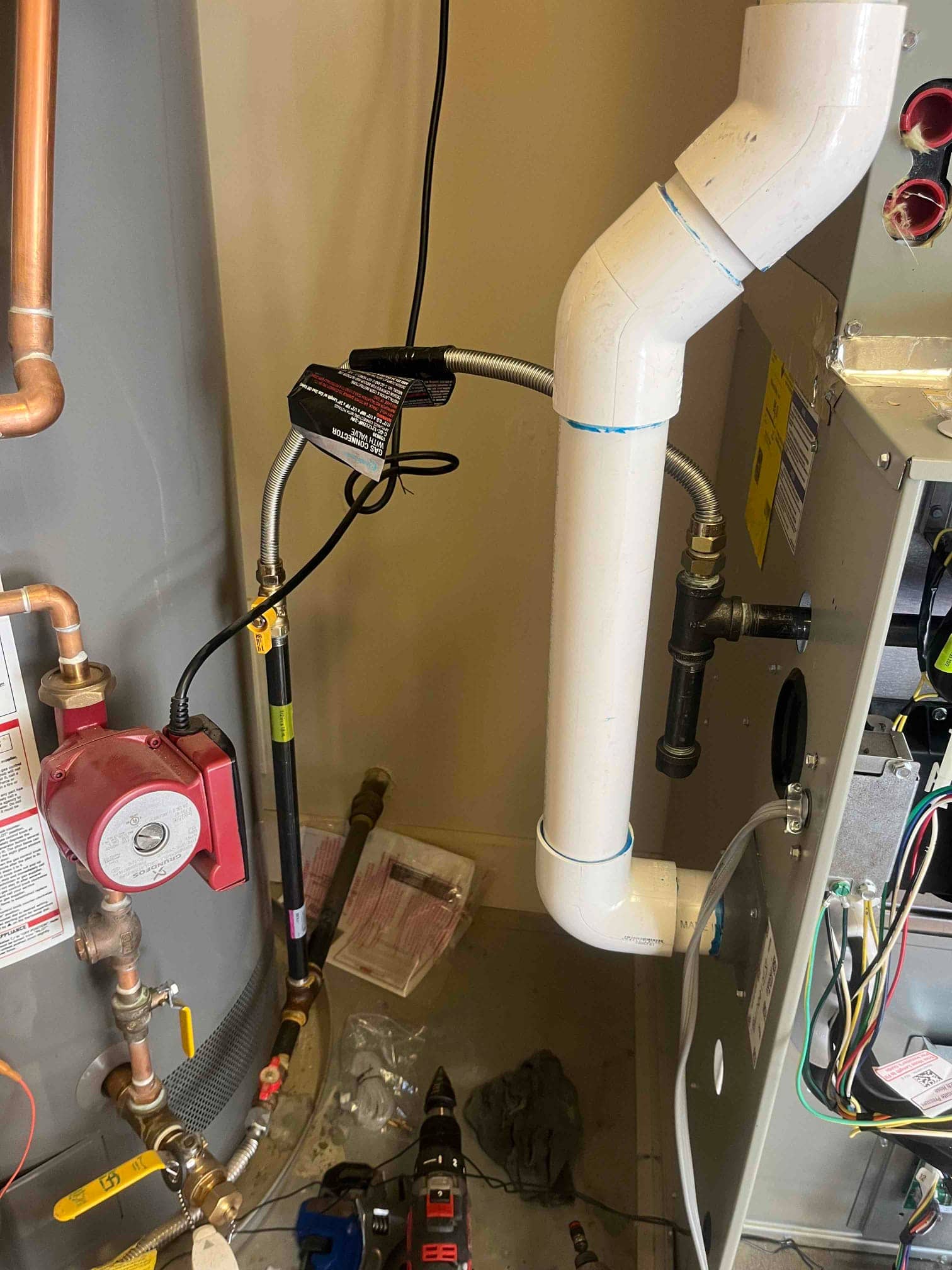 PVC condensate drain and cleanout on the furnace cabinet, with adjacent water heater, plumbing valves, and recirculation pump visible during service.