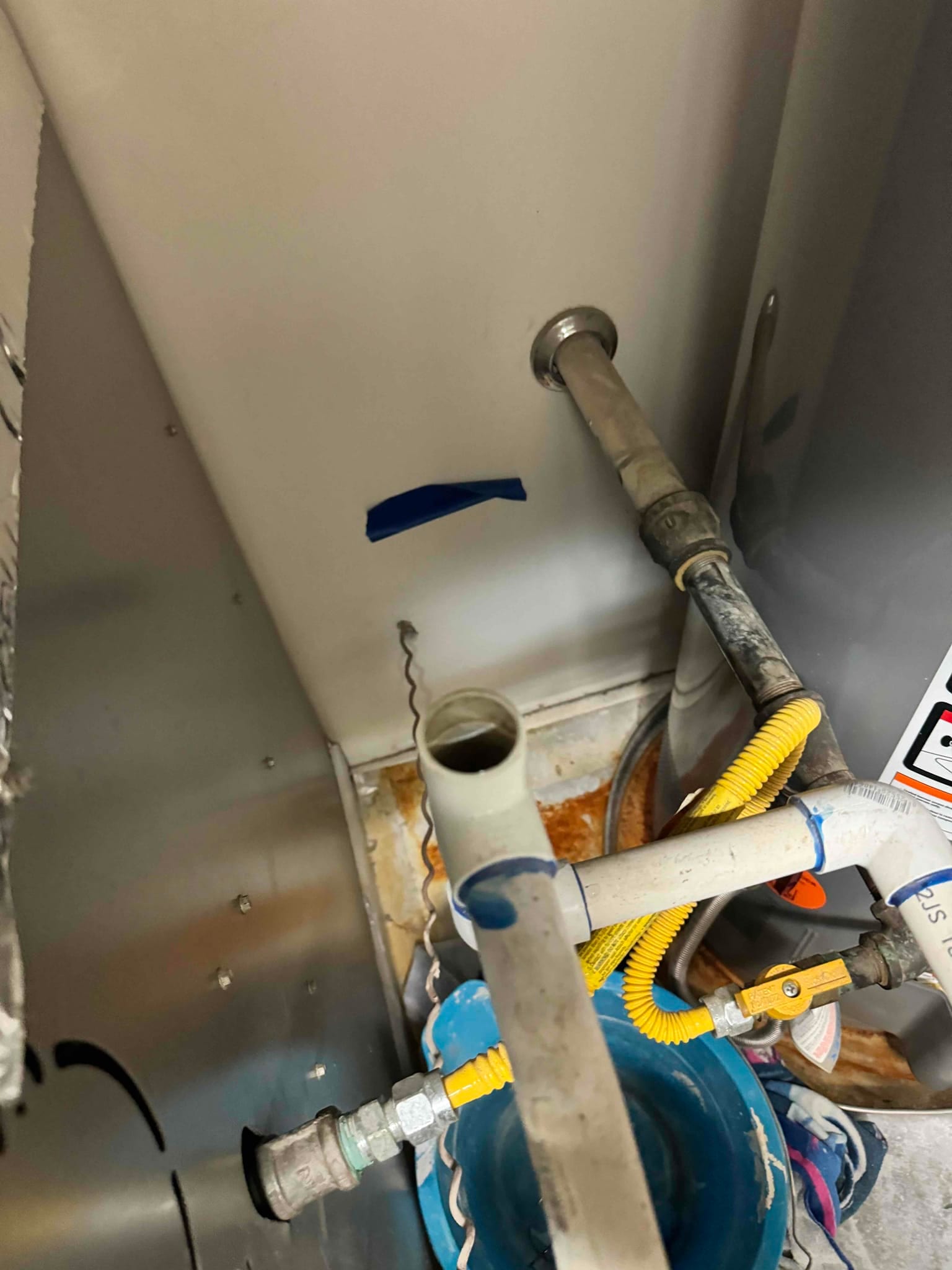 PVC condensate drain lines and yellow gas flex with shutoff valve above a rust-stained drain pan.