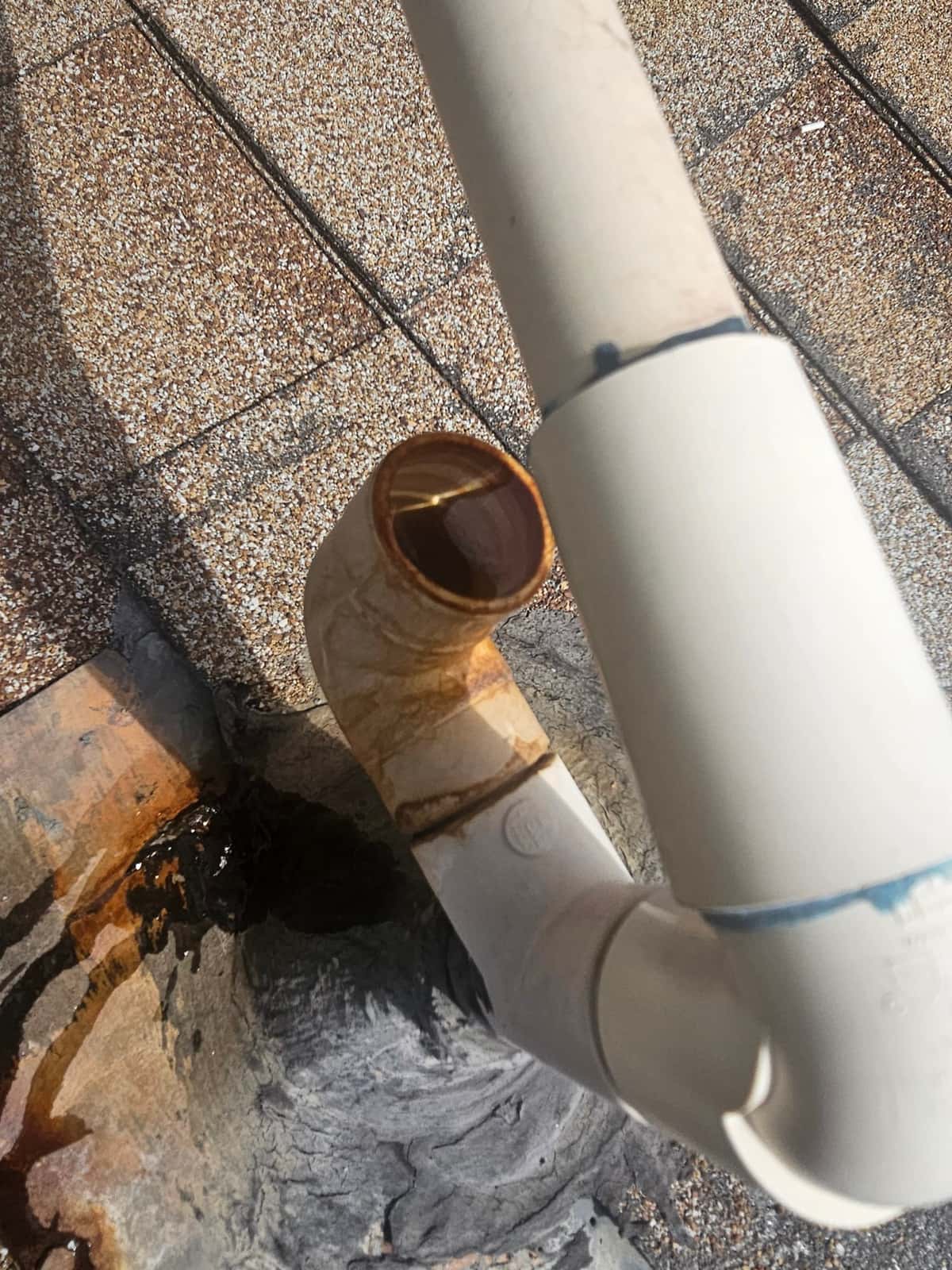PVC drain line elbow on rooftop shows brown staining at joint and wet area below outlet.