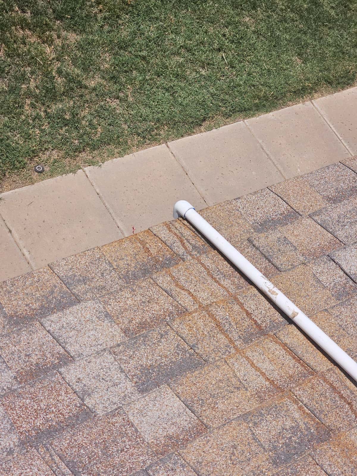 PVC drain line runs across roof shingles and terminates near the roof edge.