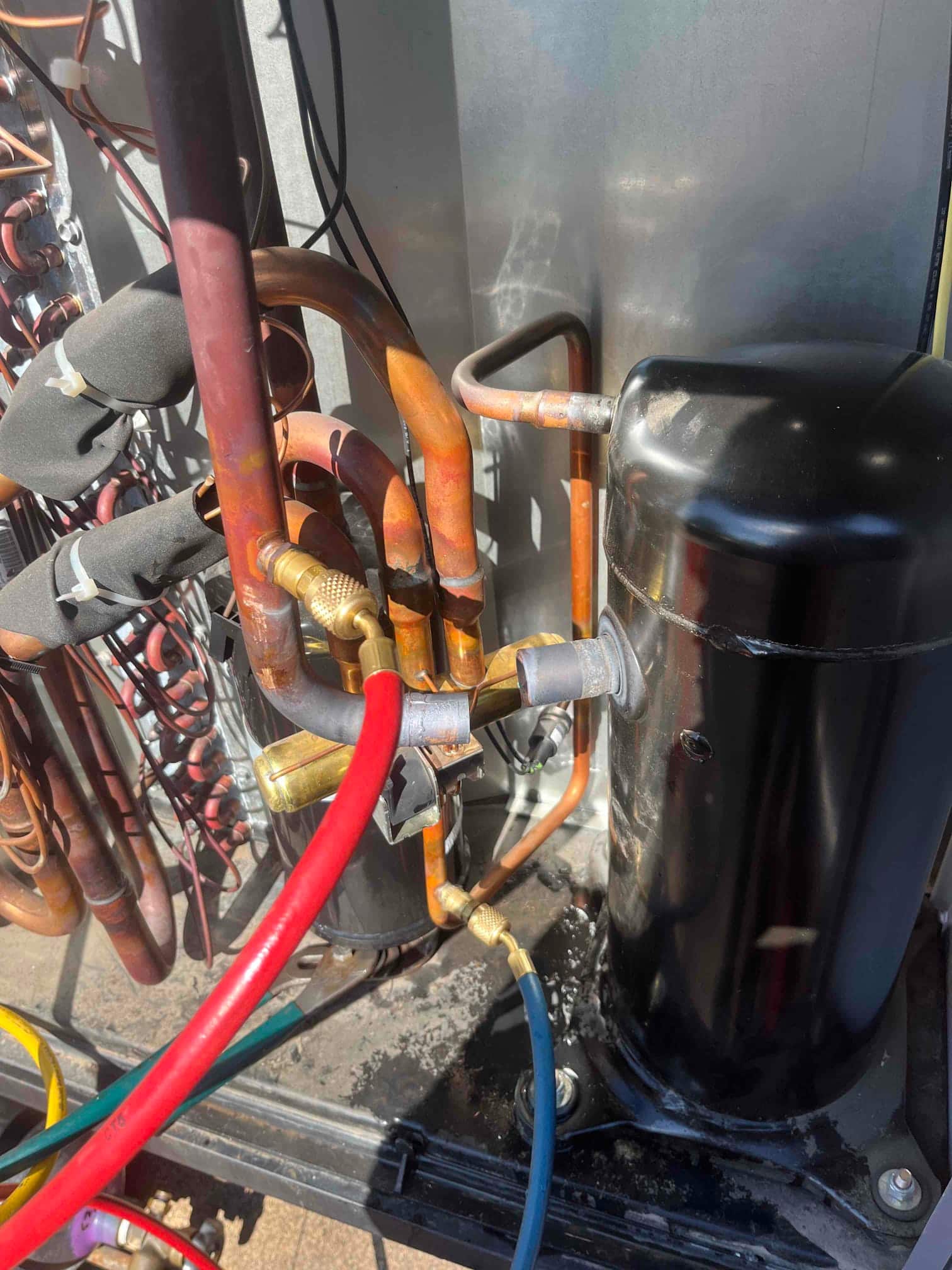 Refrigerant hoses connect to service ports on the compressor and copper lines inside the condenser unit.