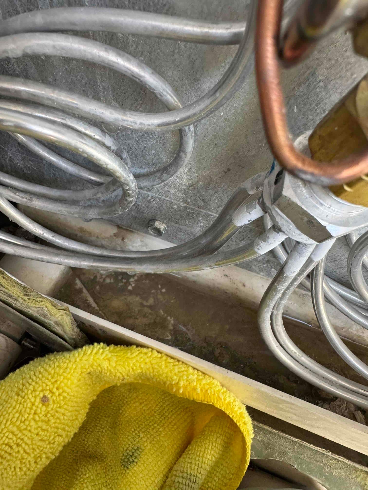 Refrigerant tubing and copper line near a brass fitting above a dirty drain pan.