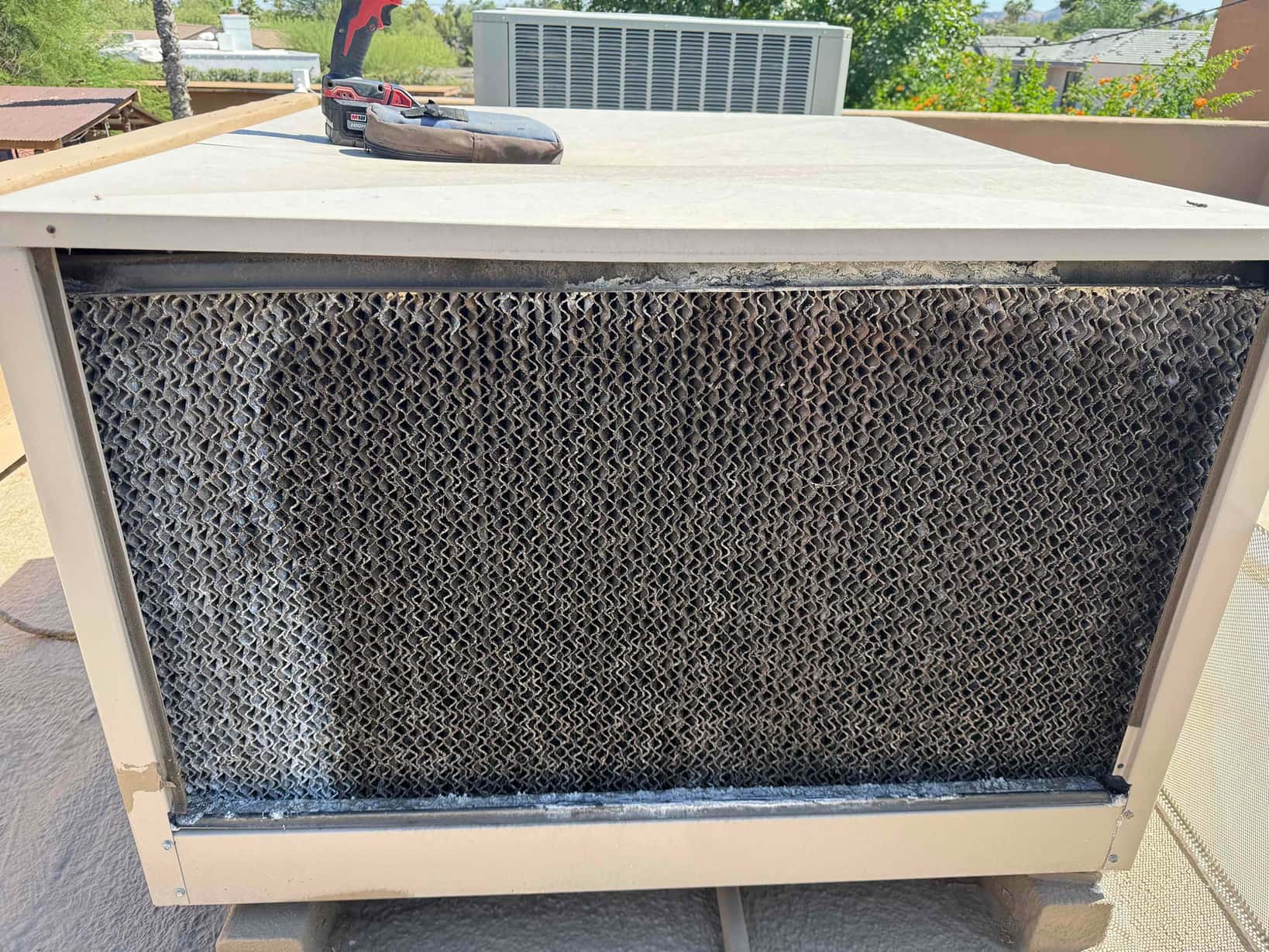 Rooftop evaporative cooler panel with honeycomb cooling pad media and mineral buildup along the bottom and left edges.