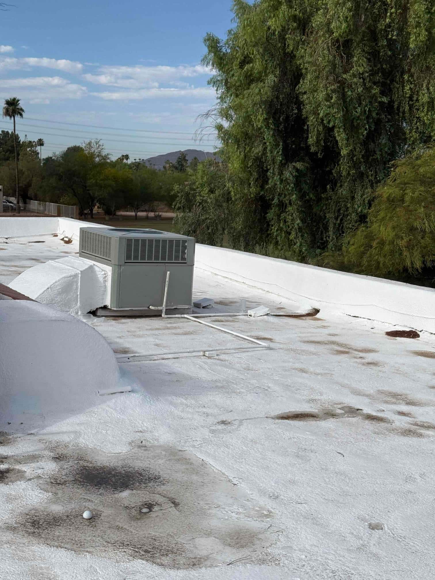 Rooftop package HVAC unit on a flat roof, with PVC condensate drain piping and surrounding roof surface.