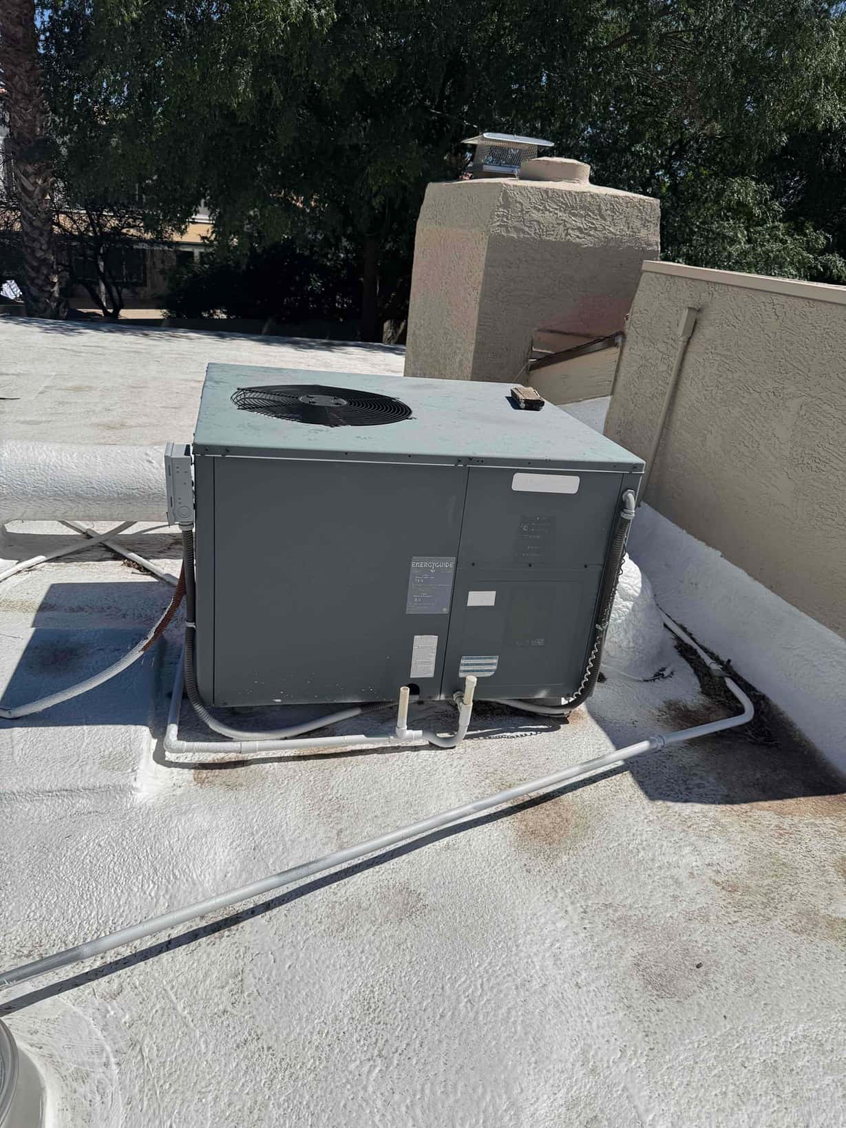 Rooftop packaged HVAC unit with supply and return duct connections and two condensate drain lines on a coated roof.