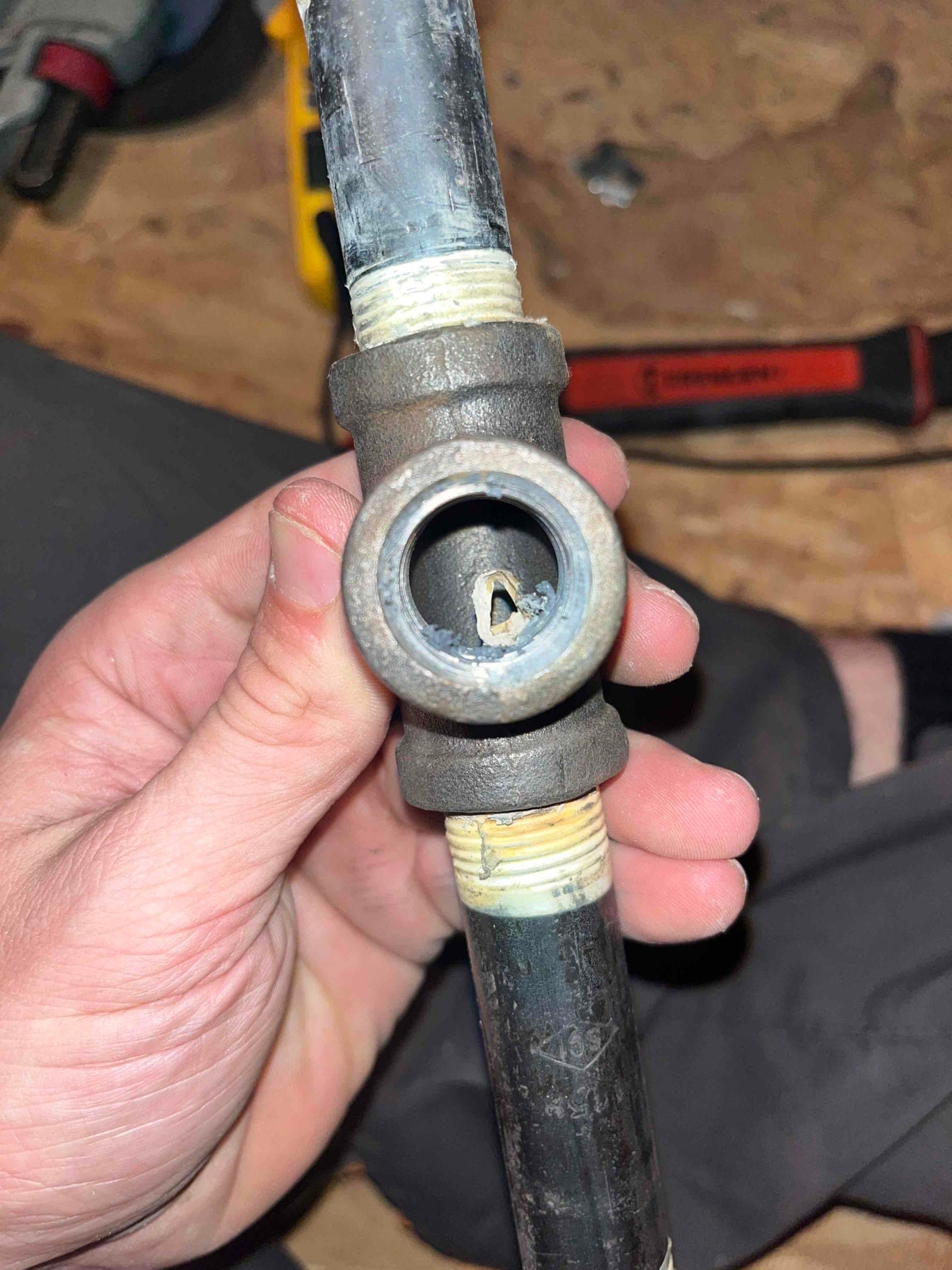 Section of black iron piping with a tee fitting; open side port shows debris inside and thread sealant on male threads.